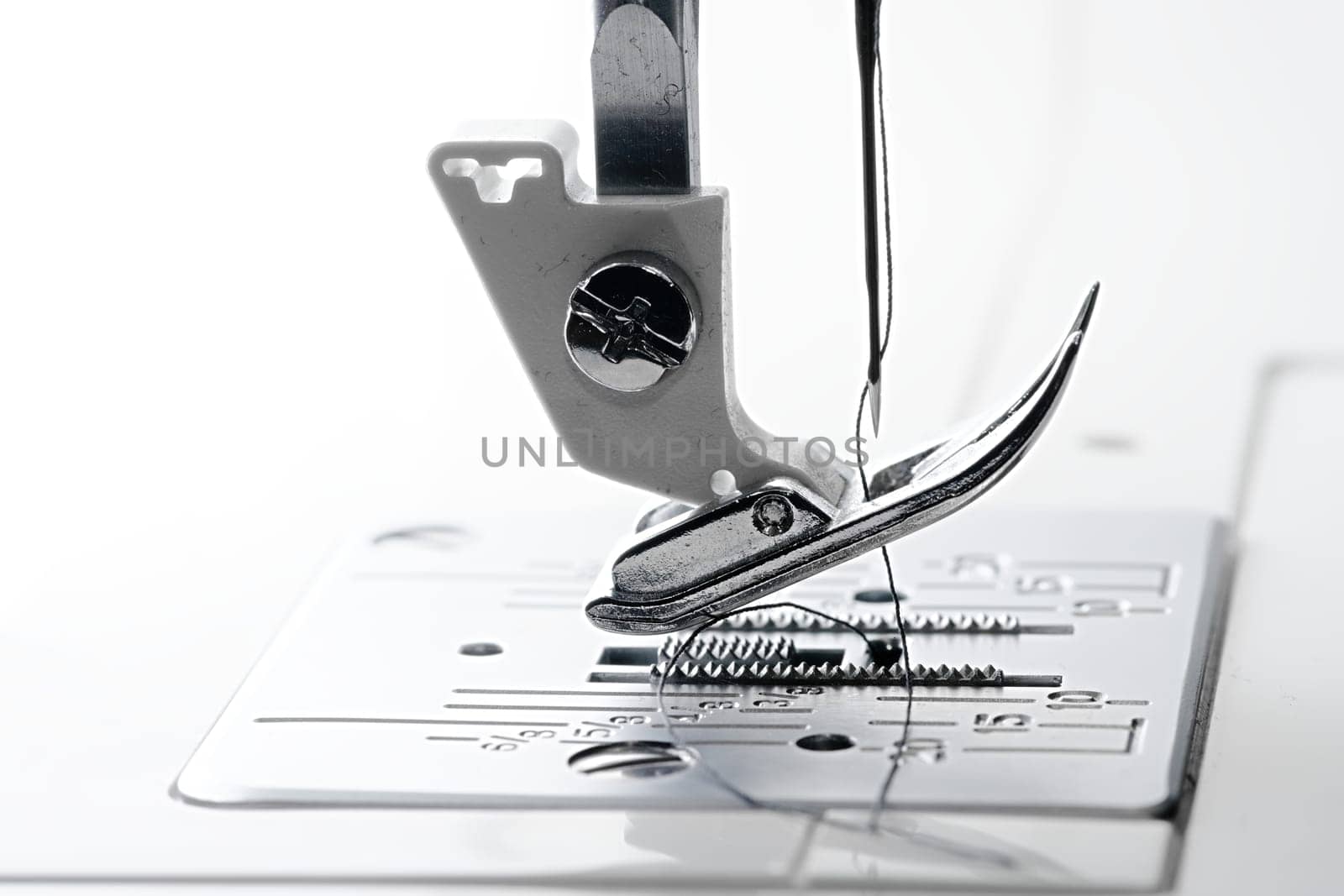 2 - Needle point and thread in macro side view of sewing machine feed dogs and throat plate.