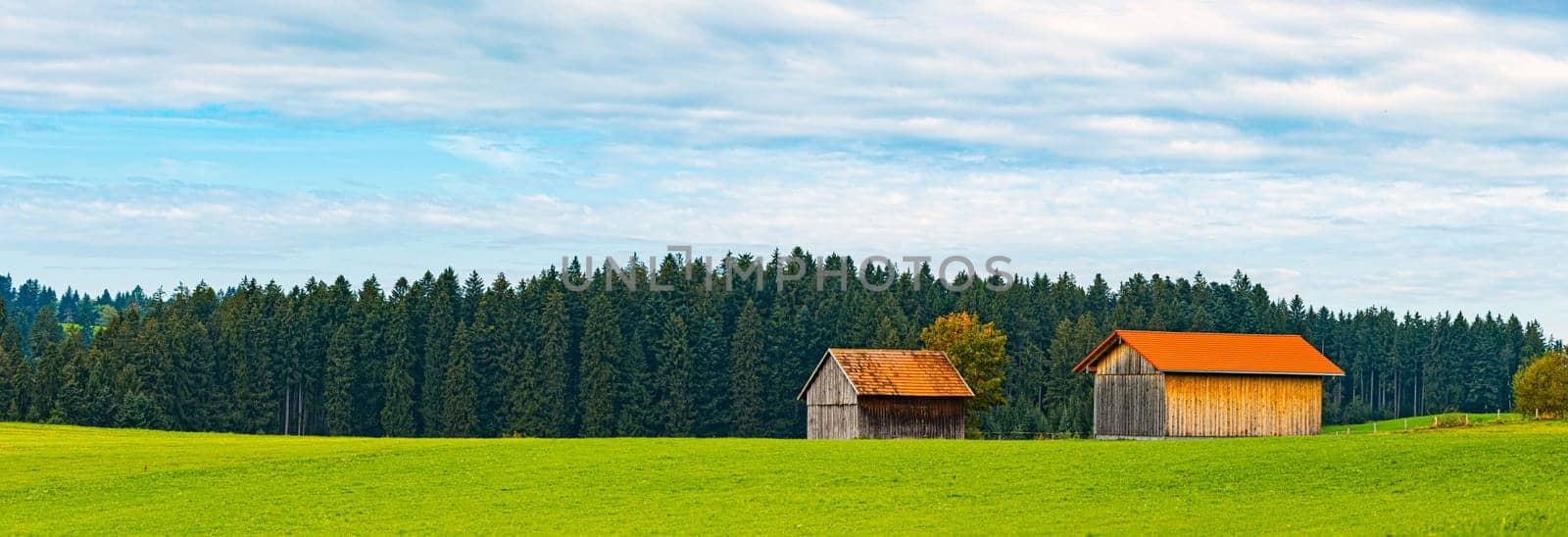 Countryside farm in Bavaria, Germany, Europe. Winding road in foreground, blue cloudy sky in background. Barns with orange tiled roofs.