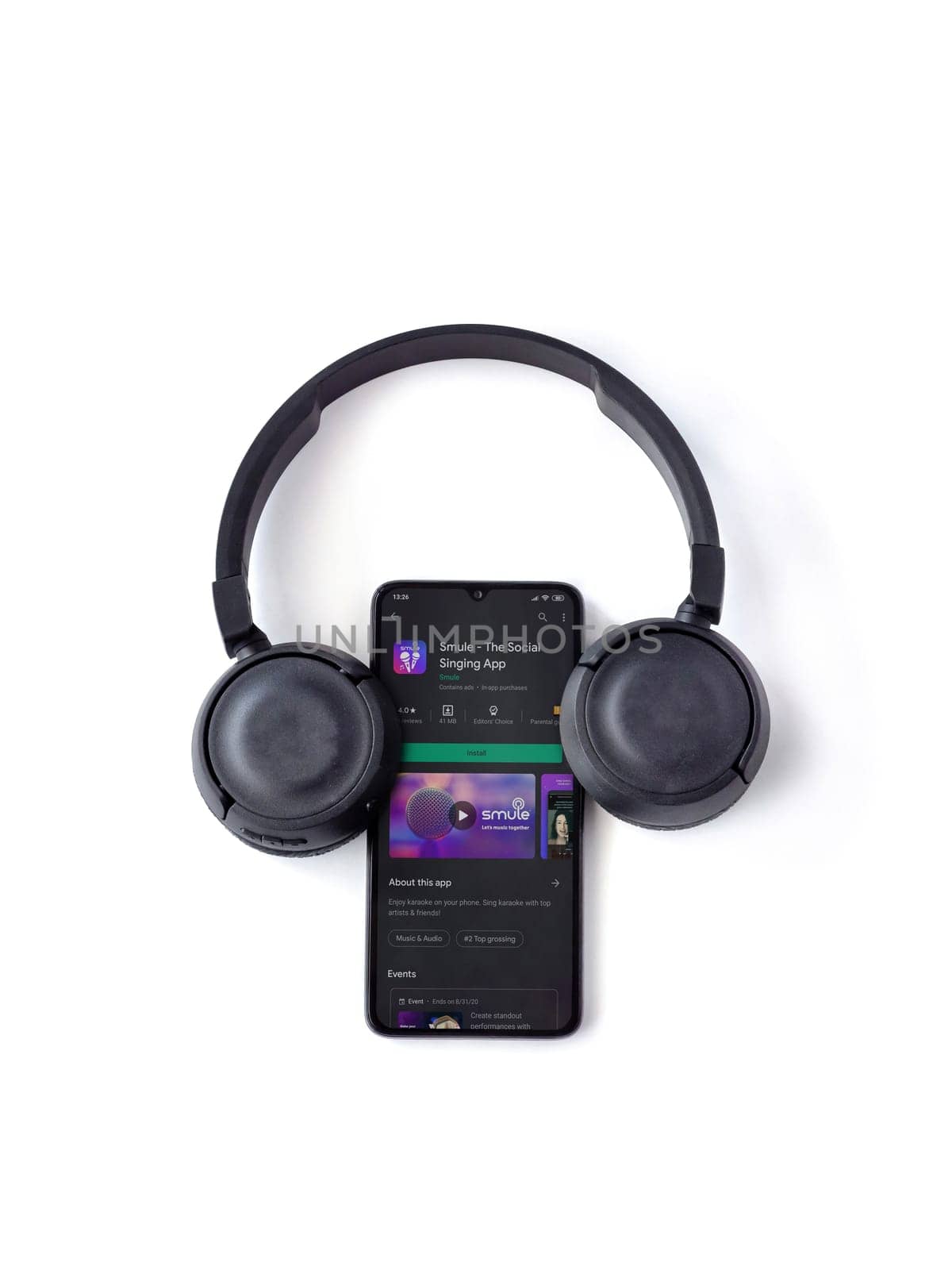 Lod, Israel - July 8, 2020: Black mobile smartphone with Smule app play store page and wireless headphones on a white background. Top view flat lay with copy space.