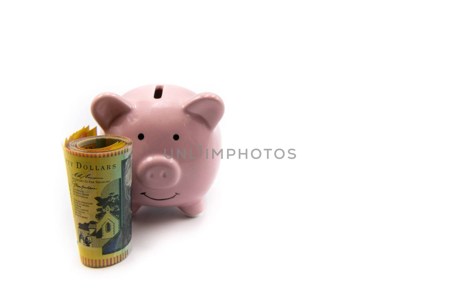 Pink piggy bank with golden crown and stack of Australian 50 dollars banknotes in front isolated over white background with copy space, cash is king concept image