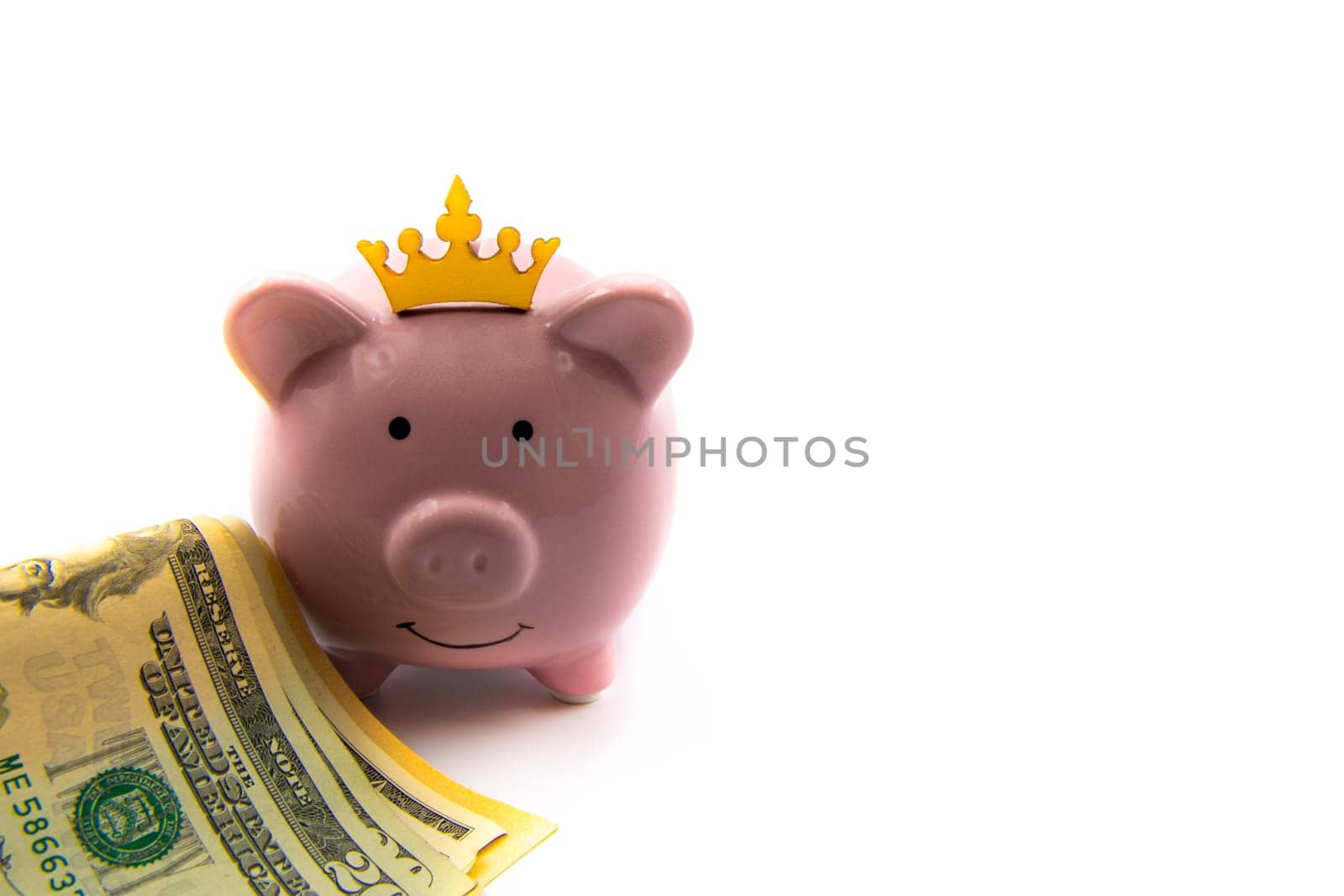 Pink piggy bank with golden crown and stack of US dollars in front isolated over white background with copy space, cash is king concept image