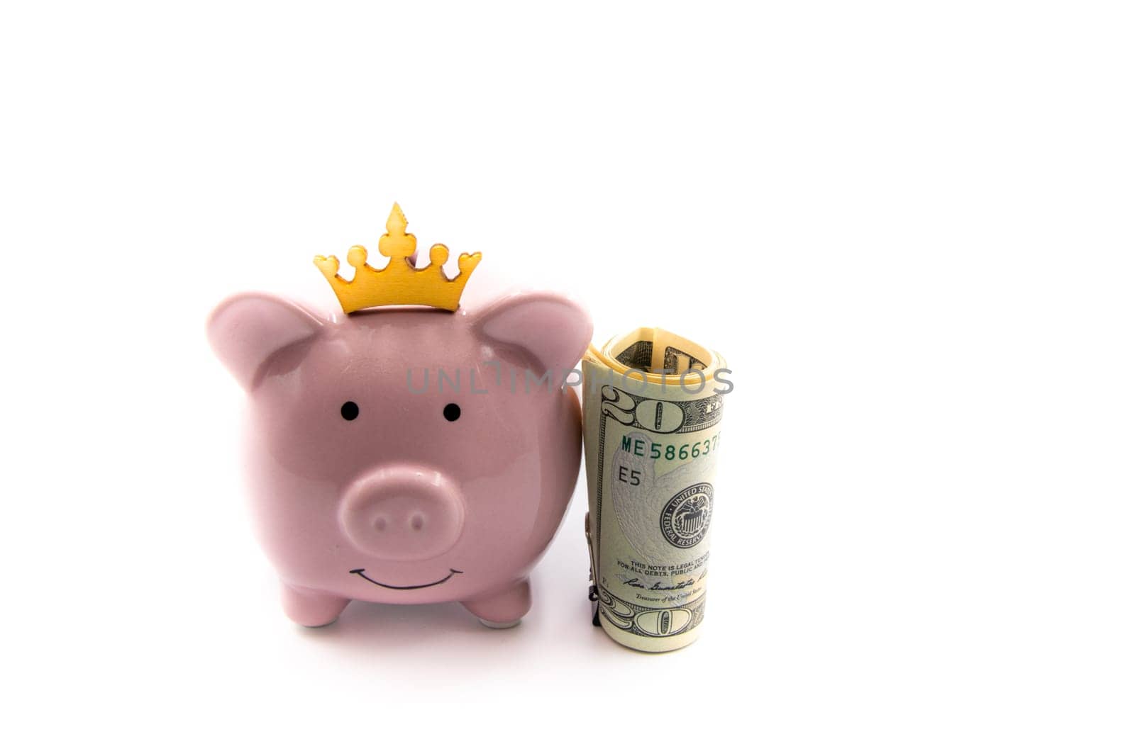 Pink piggy bank with golden crown and stack of US dollars on the right, isolated over white background with copy space, cash is king concept image