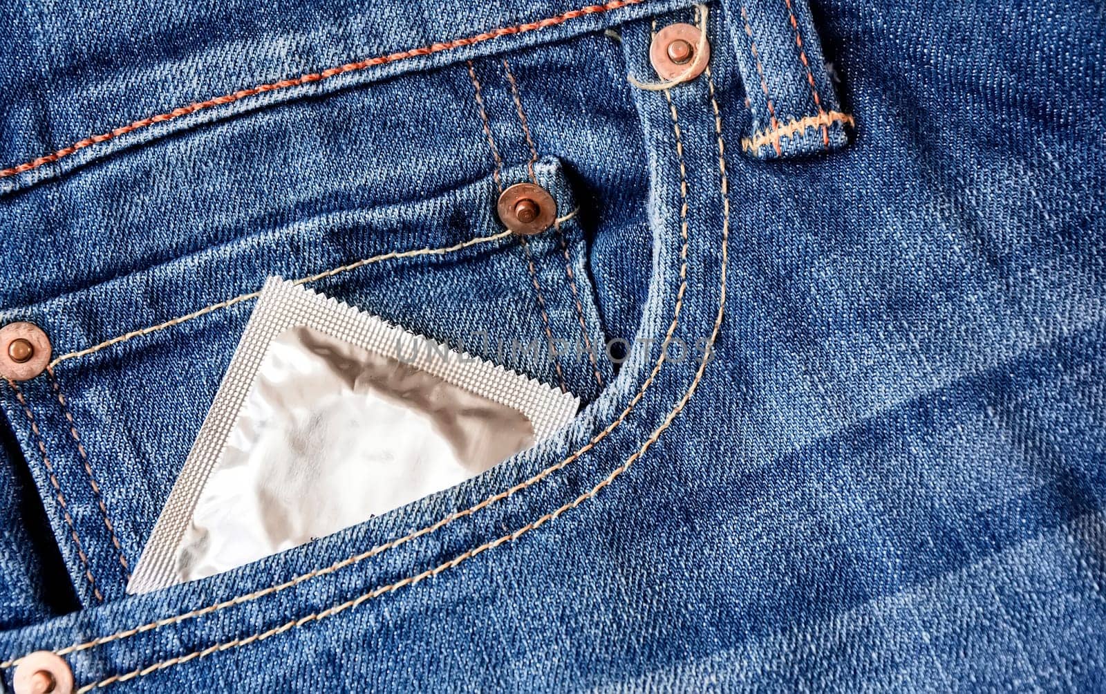 A condom pops out of the front pocket of a pair of jeans. Prevention of sexually transmitted diseases. Safe sex