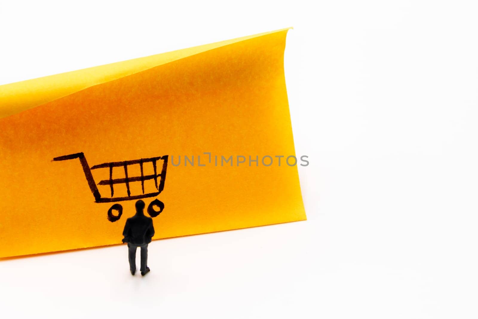 Miniature figurine posed as businessman looking at shopping cart handrawn on adhesive paper note, e-commerce concept image