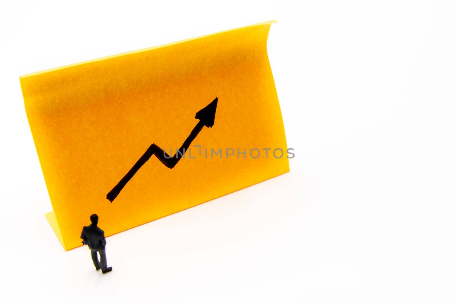 Miniature figurine posed as businessman in front of ascending graph arrow hand drawn on adhesive paper note, positive performance concept image