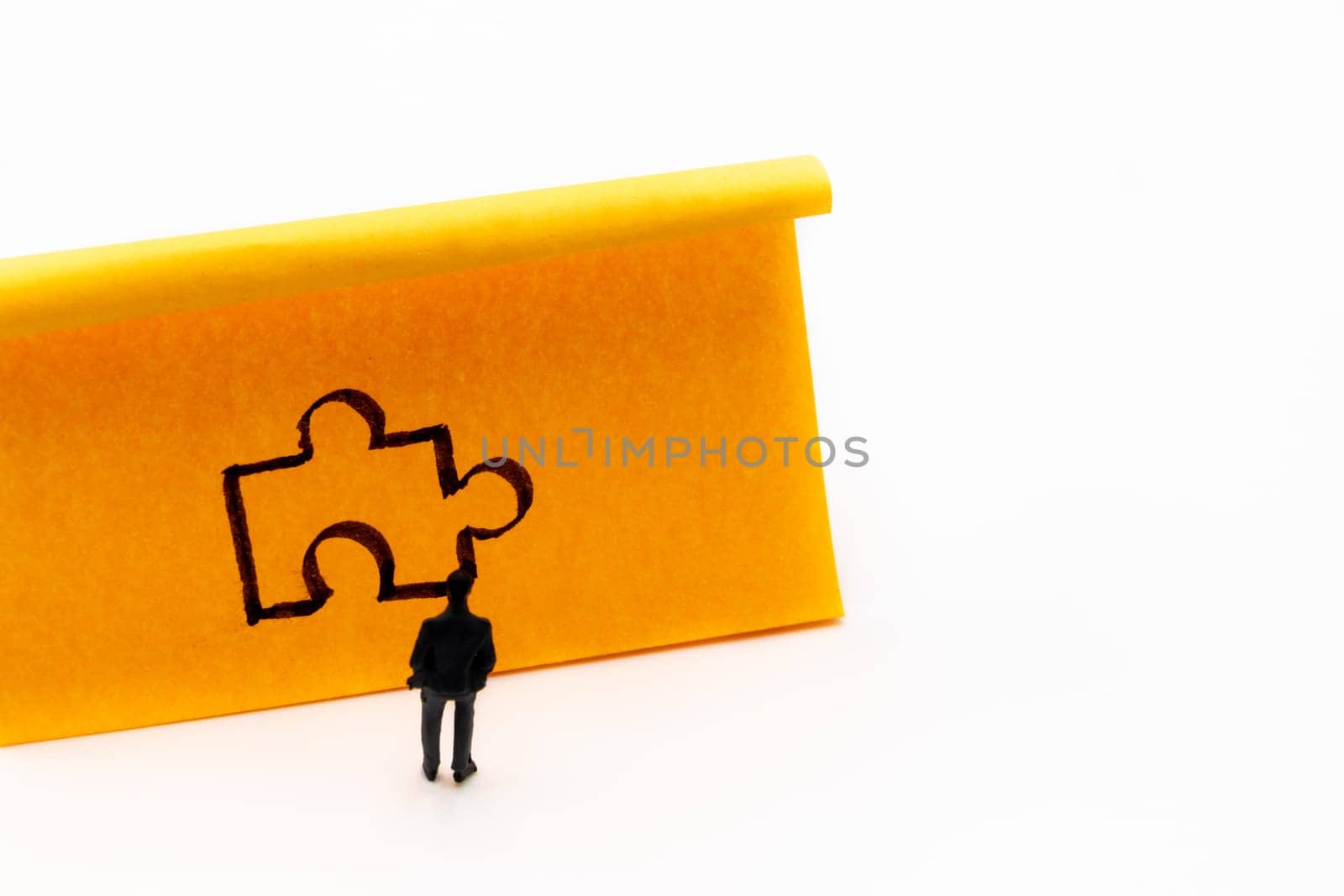 Miniature figurine posed as businessman in front of handrawn puzzle piece on adhesive paper note, solution concept image