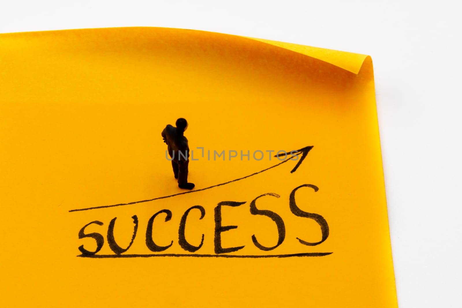 Miniature figurine posed as businessman on ascending graph arrow with Success growth text handwritten on adhesive paper note, positive performance concept image