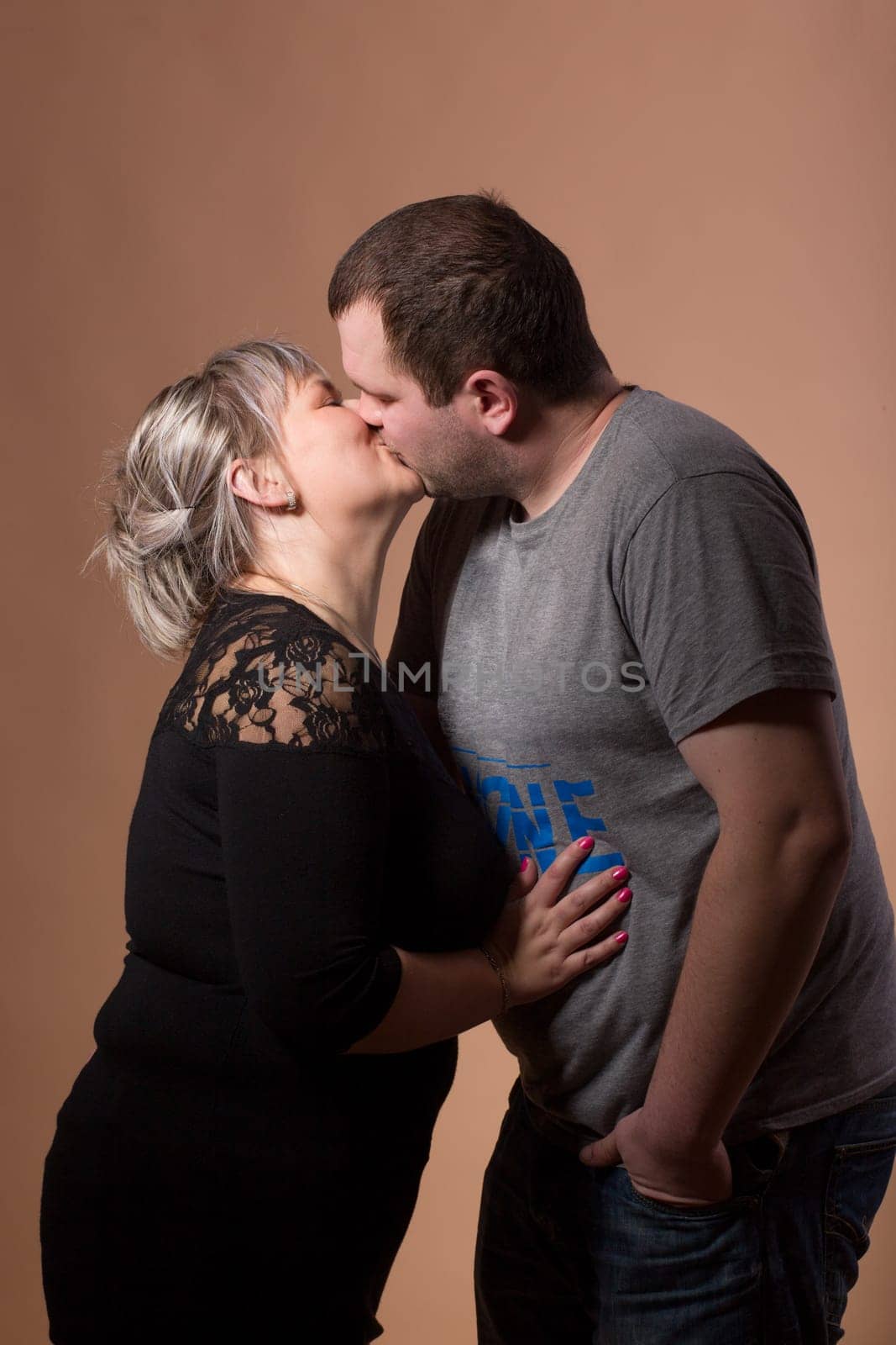 Studio shoot of beautiful fashion xxl woman kissing her husband, happy couple love concept