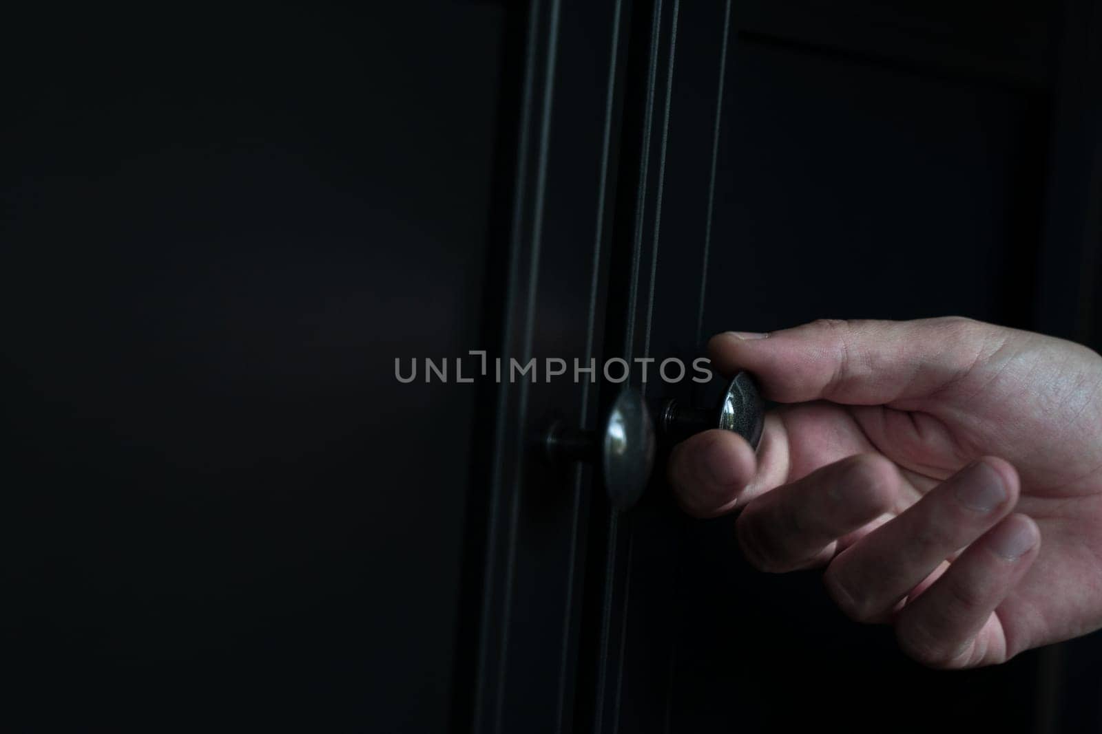 perspective side view closeup of Caucasian man hand opening a wooden closed black clothes dresser cabinet with a metallic door knob