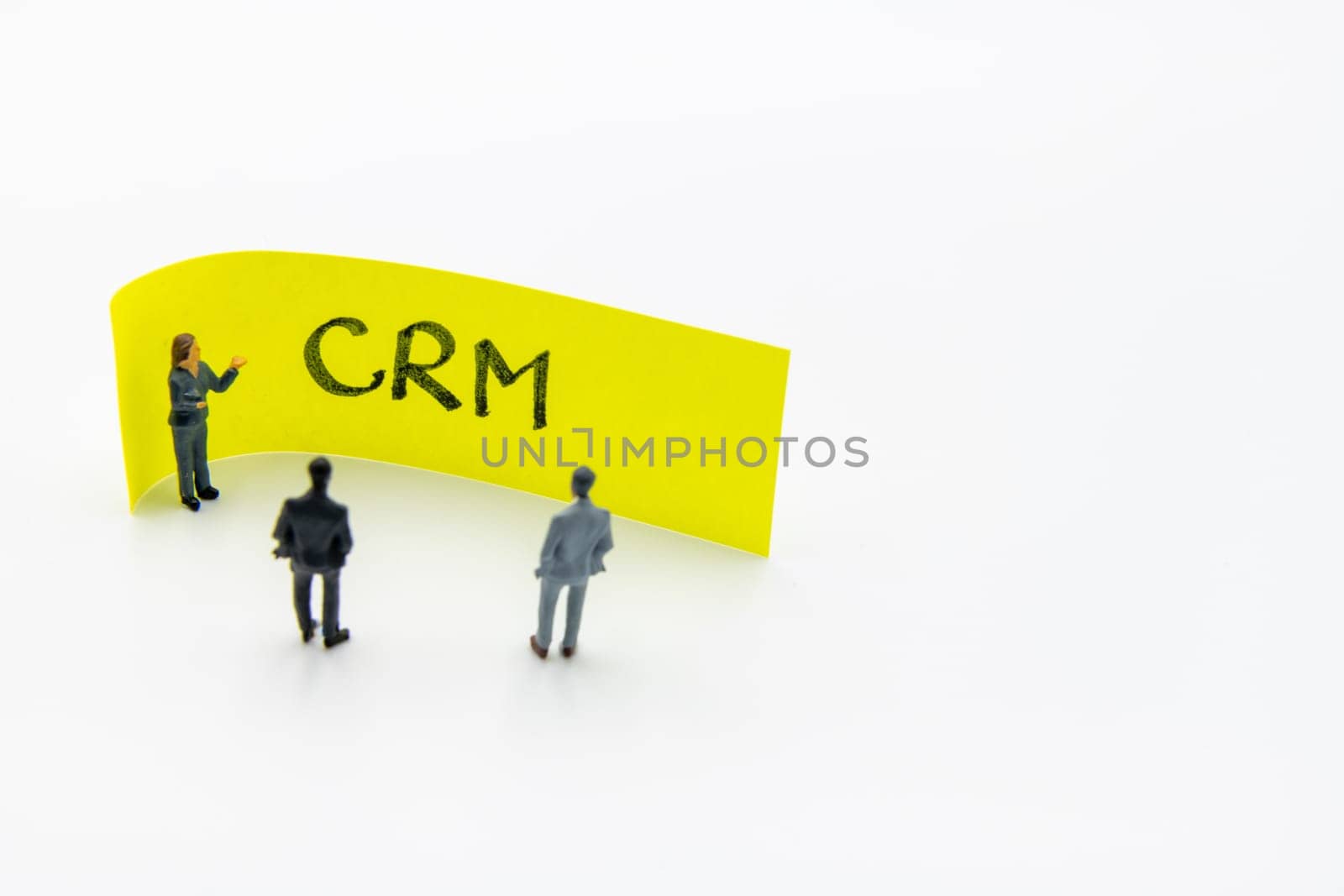 Presentation meeting with miniature figurines posed as business people standing in front of post-it note with CRM Customer Relationship Management handwritten message in background