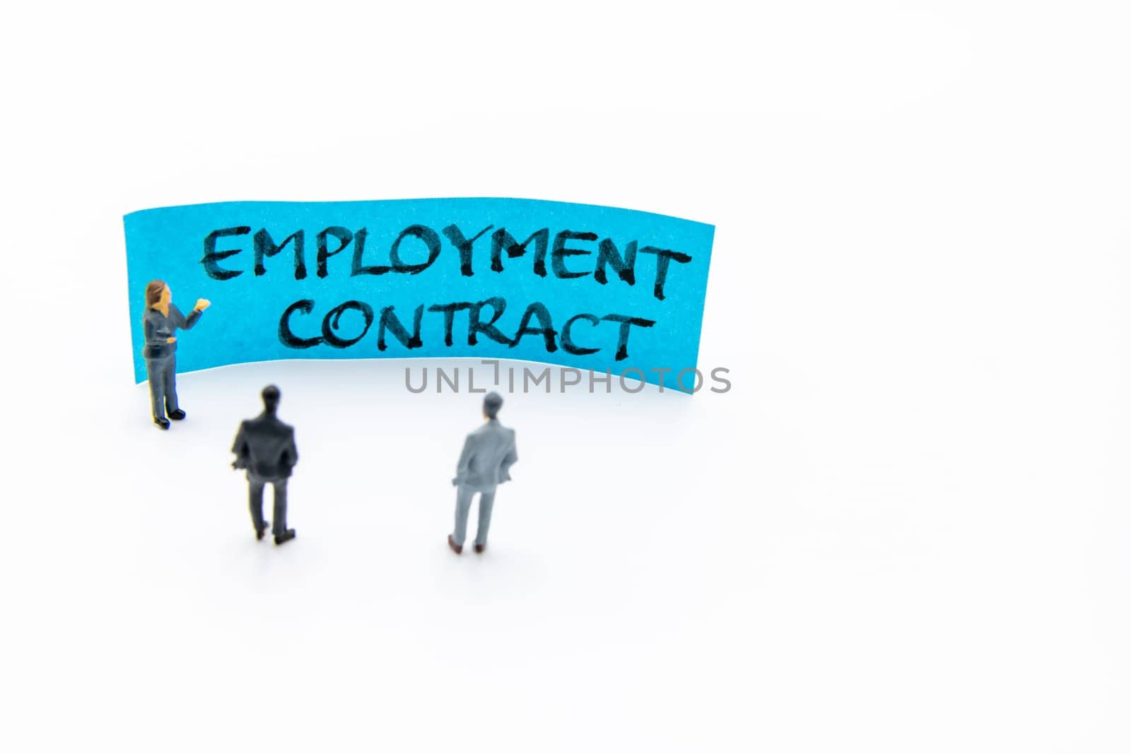 Presentation meeting with miniature figurines posed as business people standing in front of post-it note with Employment Contract handwritten message in background, copy space on the right