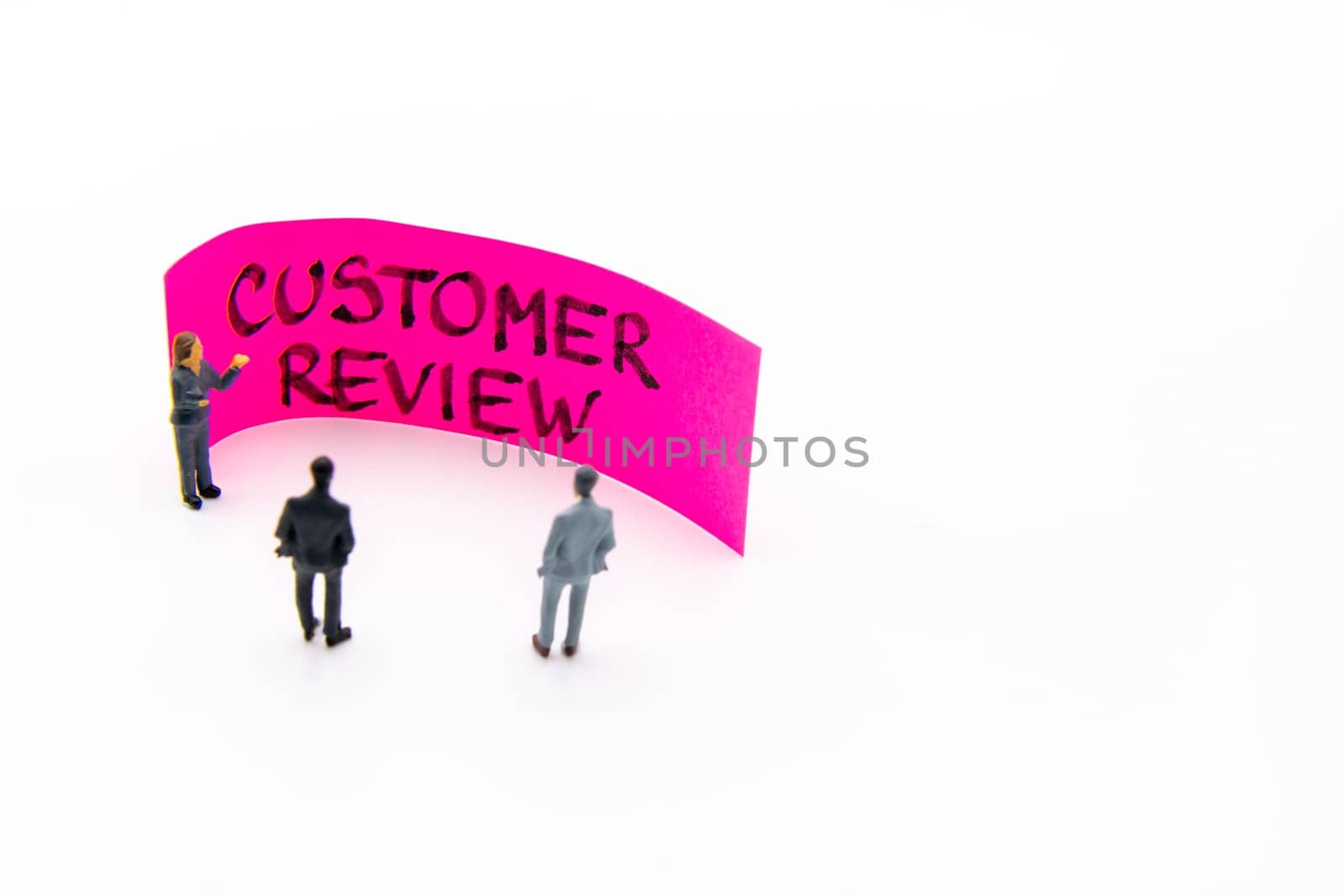 Presentation meeting with miniature figurines posed as business people standing in front of post-it note with Customer Review handwritten message in background, copy space on the right