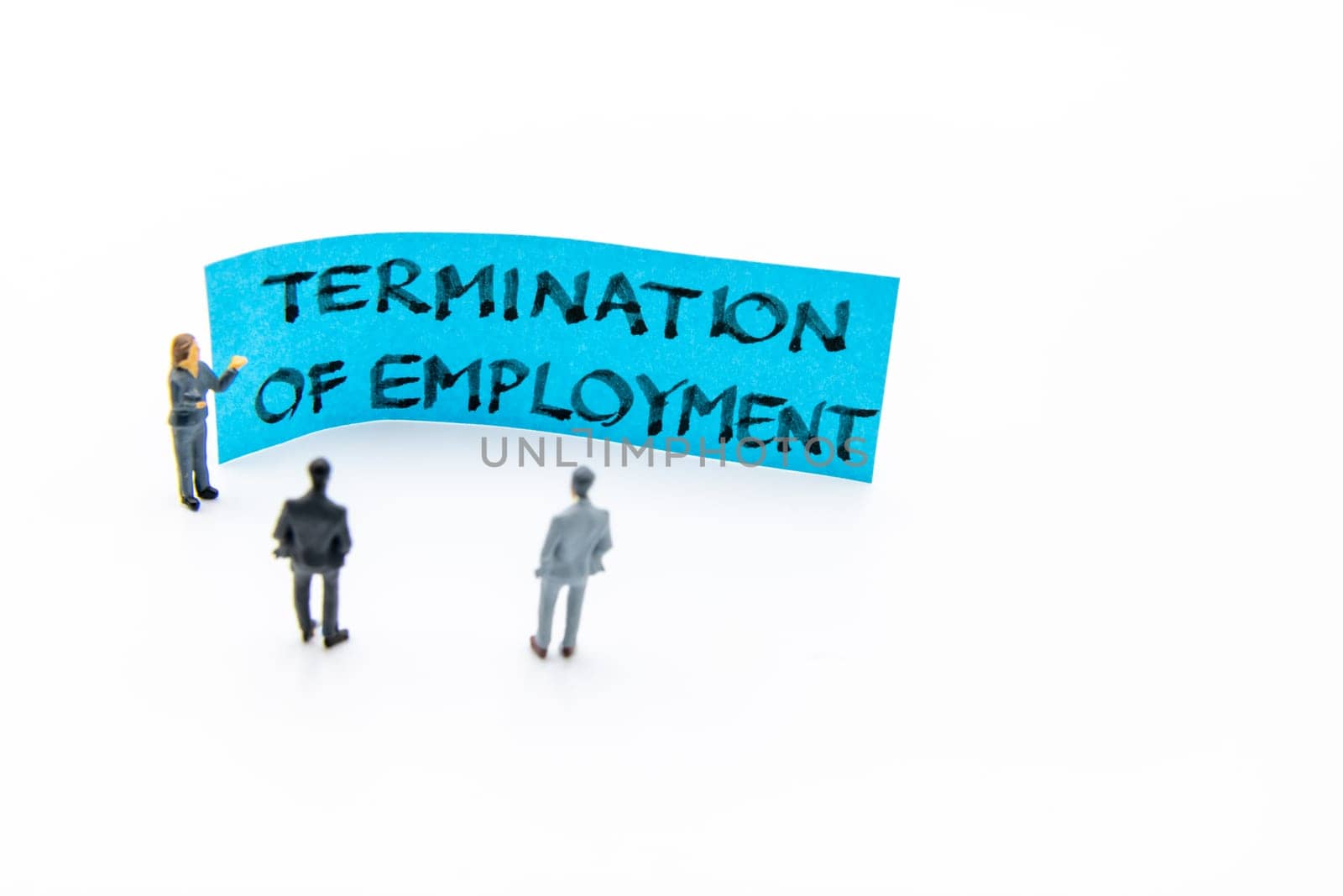 Presentation meeting with miniature figurines posed as business people standing in front of post-it note with Termination of Employment handwritten message in background, copy space on the right
