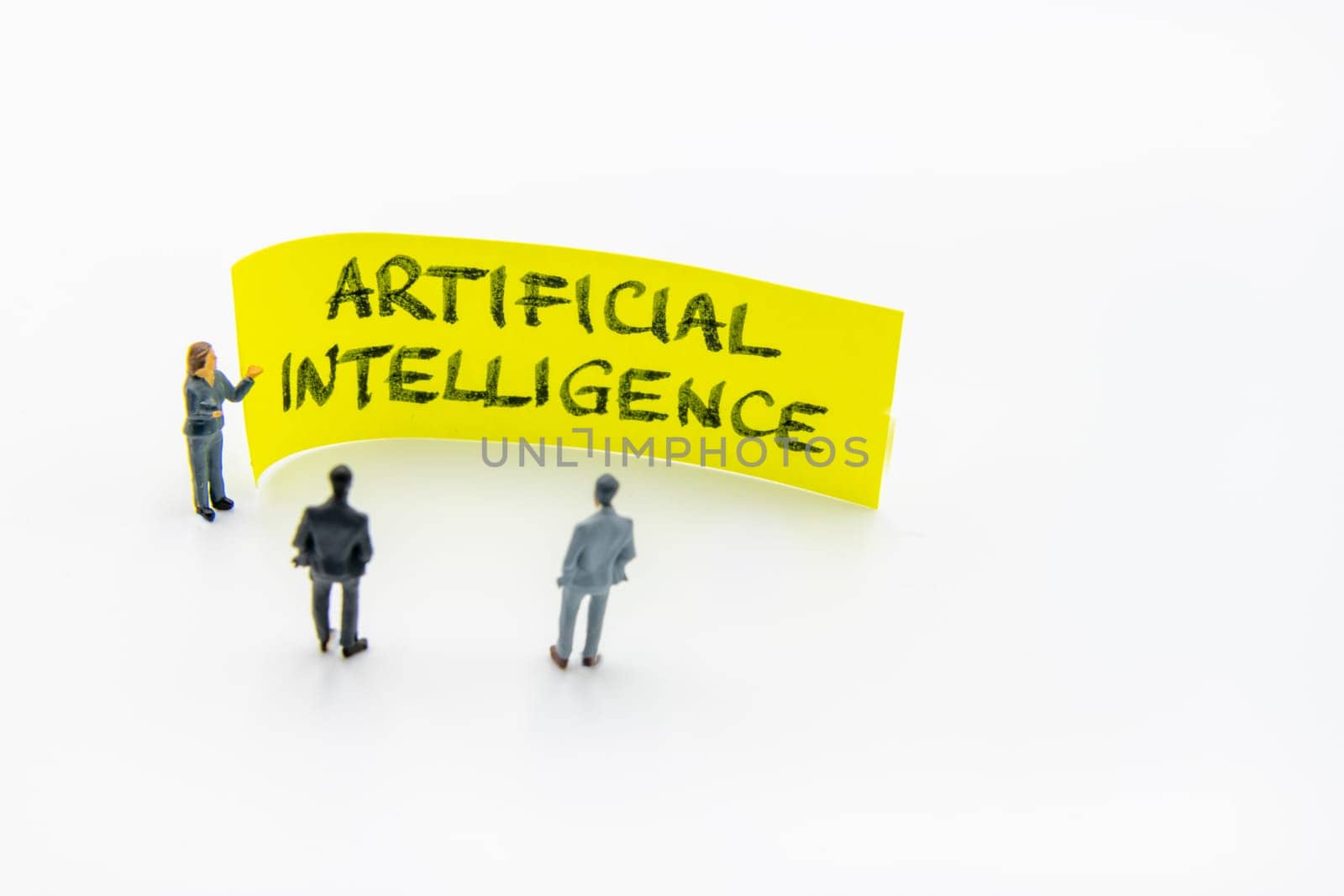 Presentation meeting with miniature figurines posed as business people standing in front of post-it note with Artificial Intelligence handwritten message in background, copy space on the right