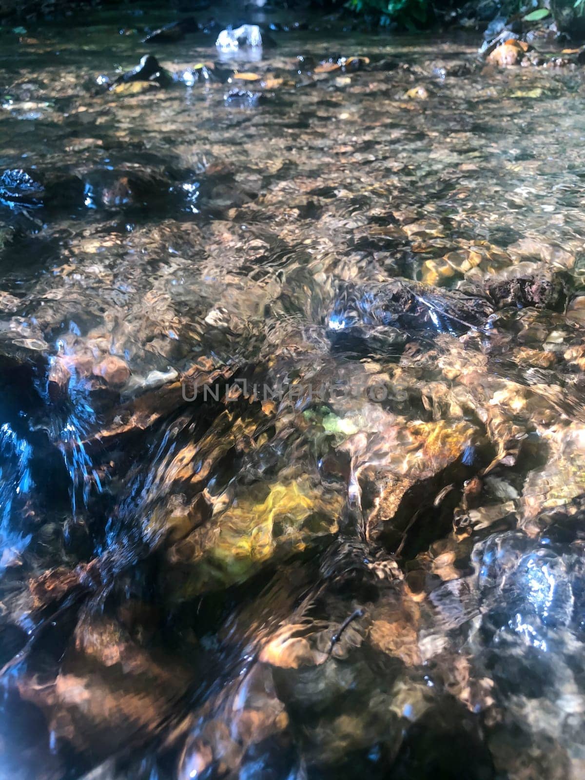 Trippy image of swirls curves and ripples of moving water over colorful stones. Peaceful and serene nature background.