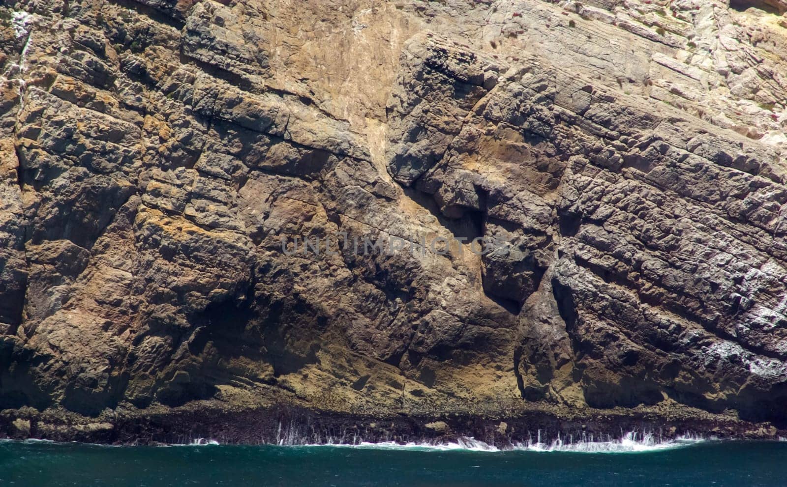gorgeous massive cliff with ocean waves crashing its base. Beautiful colors and texture.