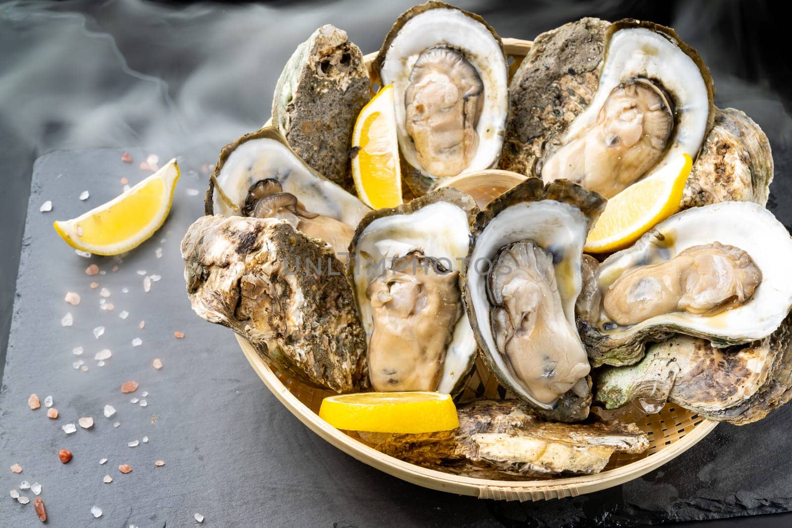 Fresh oyster serve with lemon in basket on black stone plate. Fresh seafood food and european cuisine gourmet concept.