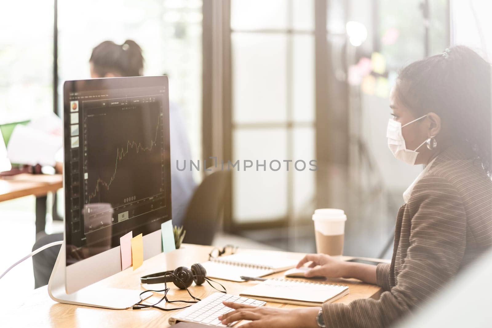 Mixed race of African black and asian businesswoman office worker wear protective face mask working in new normal office with social distance between table to prevent coronavirus COVID-19 spreading.