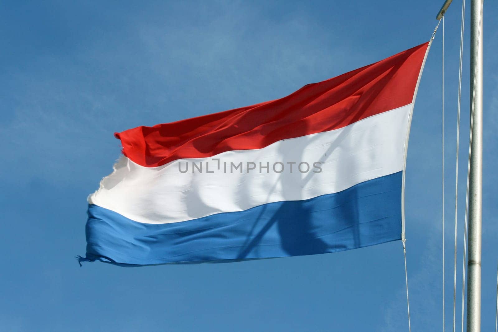 Flag of the Netherlands with blue sky in the background.