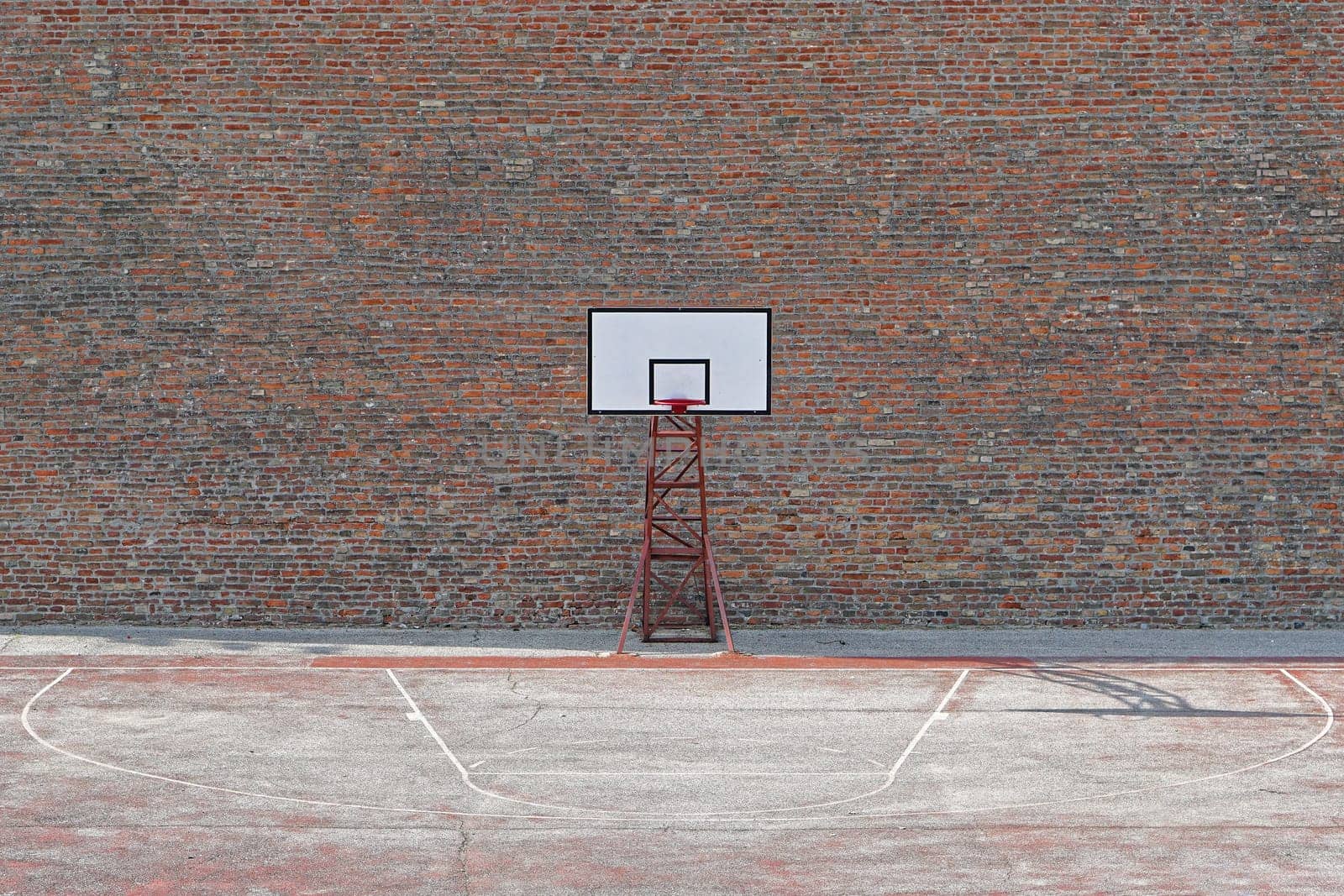 Basketball court with one hoop in front of brick wall