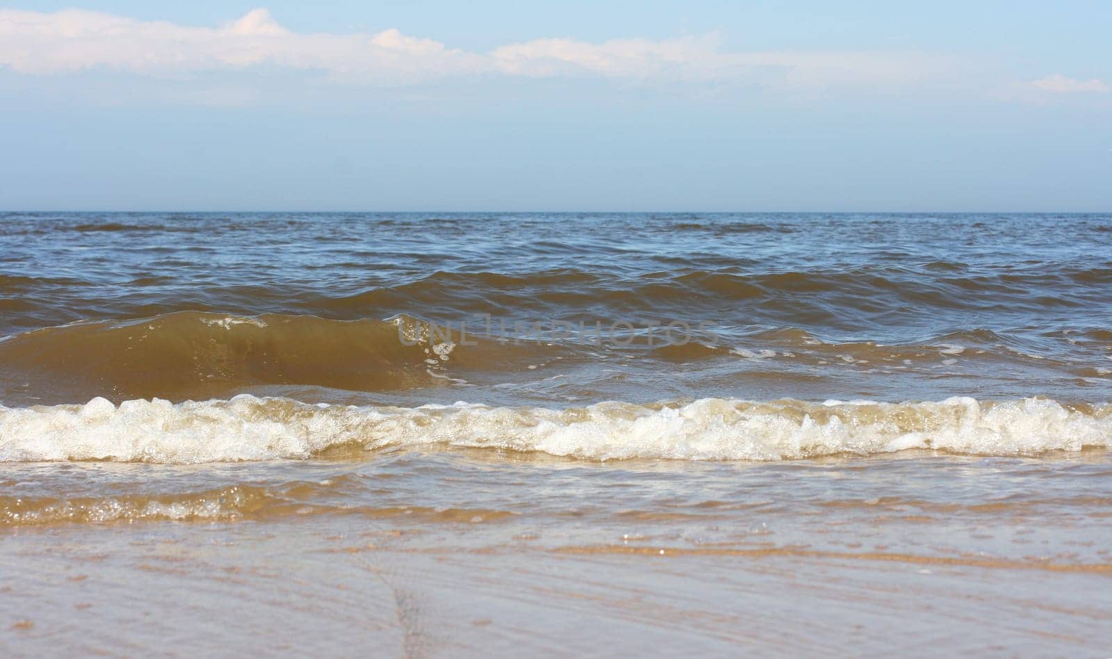 Waves with whitecaps flood the sandy beach.