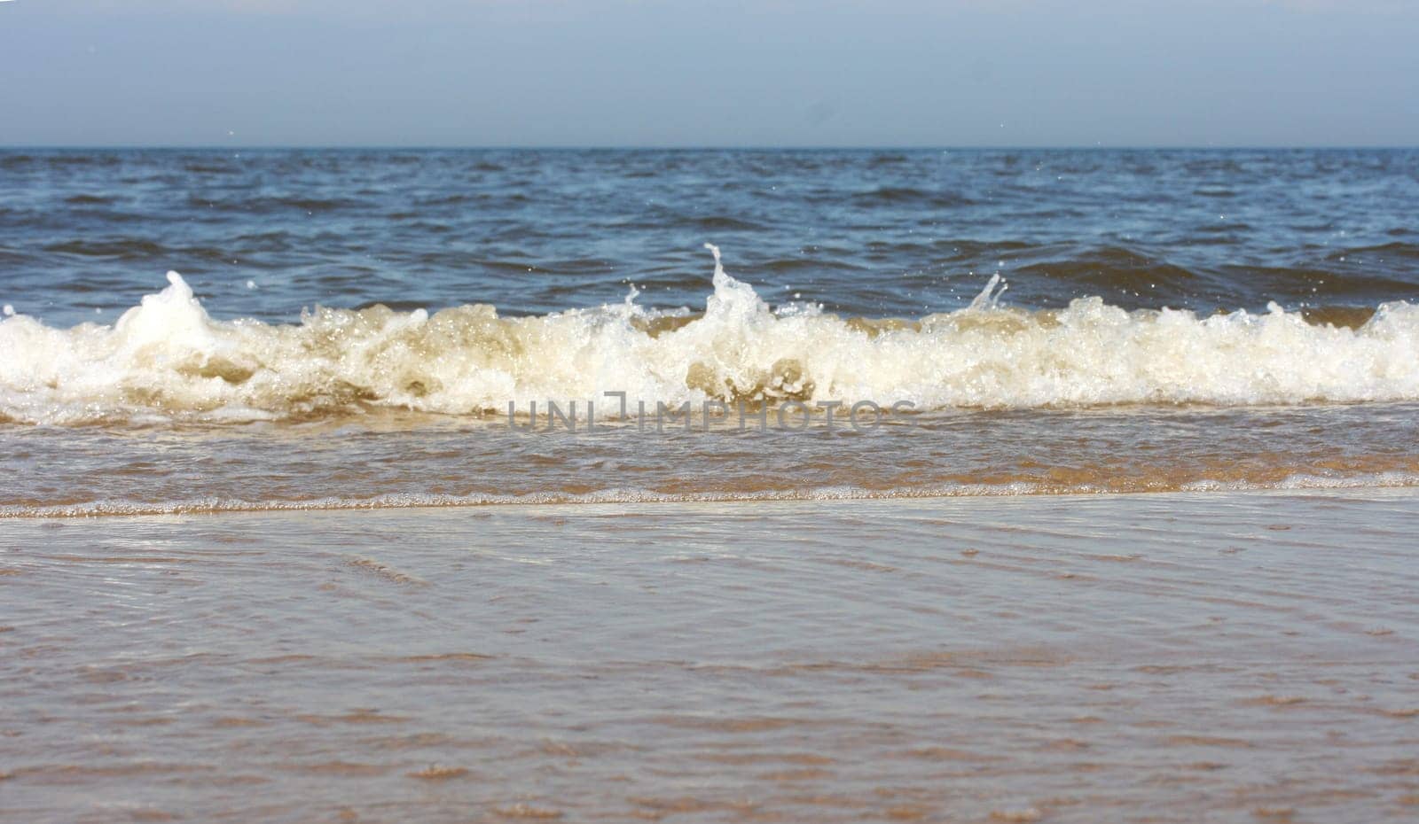 Waves with whitecaps flood the sandy beach.