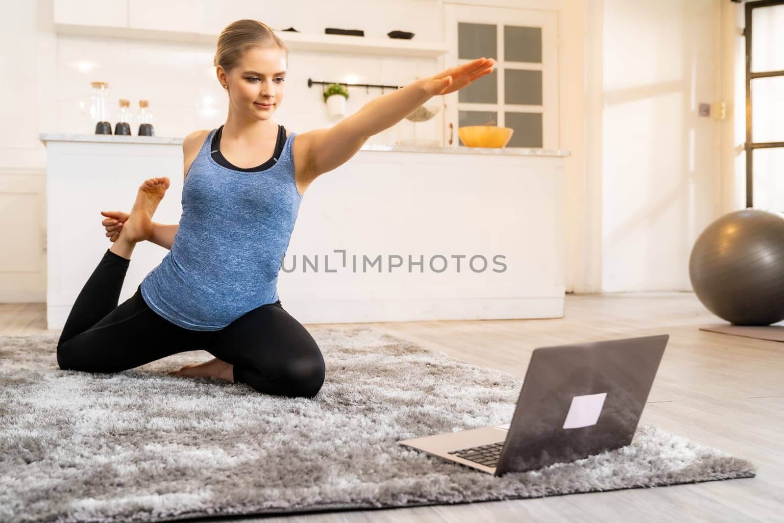 White caucasian fit sporty woman doing yoga king pigeon pose while working at home with laptop in living room while quarantine. Workout fitness sport healthy lifestyle and work from home concept.