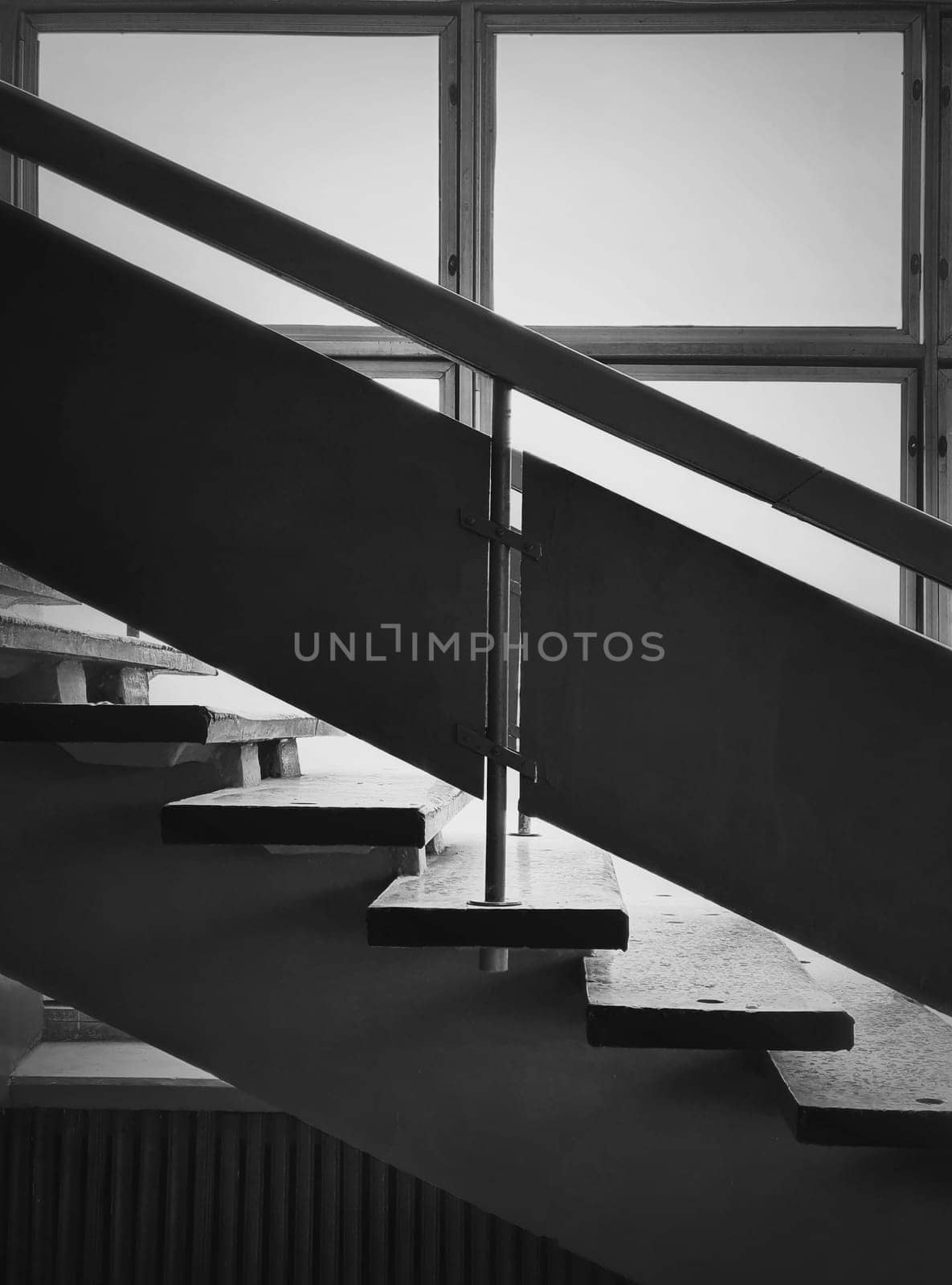 Black and white interior architecture details, old staircase by the window. Wooden railing and stone stair steps inside a shabby building. Aged construction structure elements. Vertical photo.