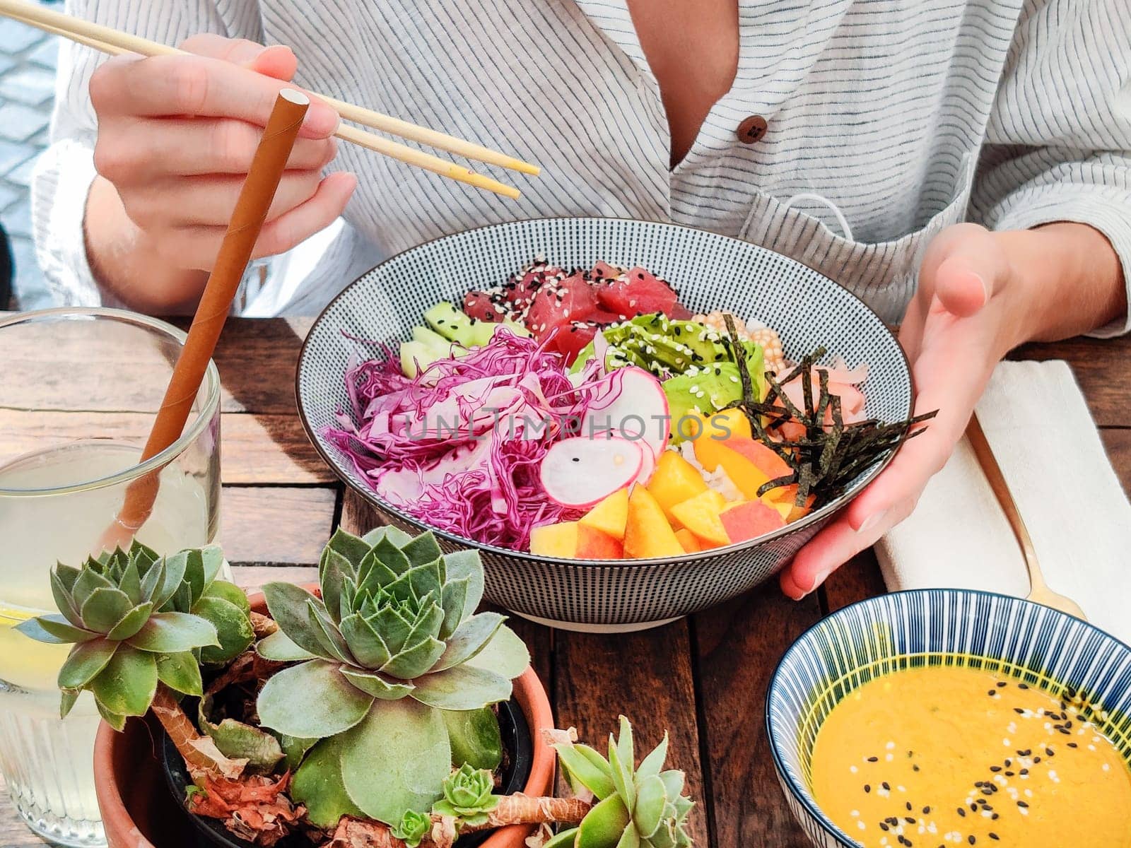 Woman eating tasty colorful healthy natural organic vegetarian Hawaiian poke bowl using asian chopsticks on rustic wooden table. Healthy natural organic eating concept.