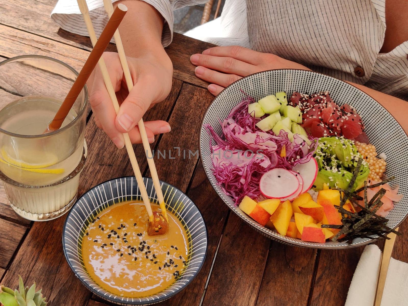 Woman eating tasty colorful healthy natural organic vegetarian Hawaiian poke bowl using asian chopsticks on rustic wooden table. Healthy natural organic eating concept.