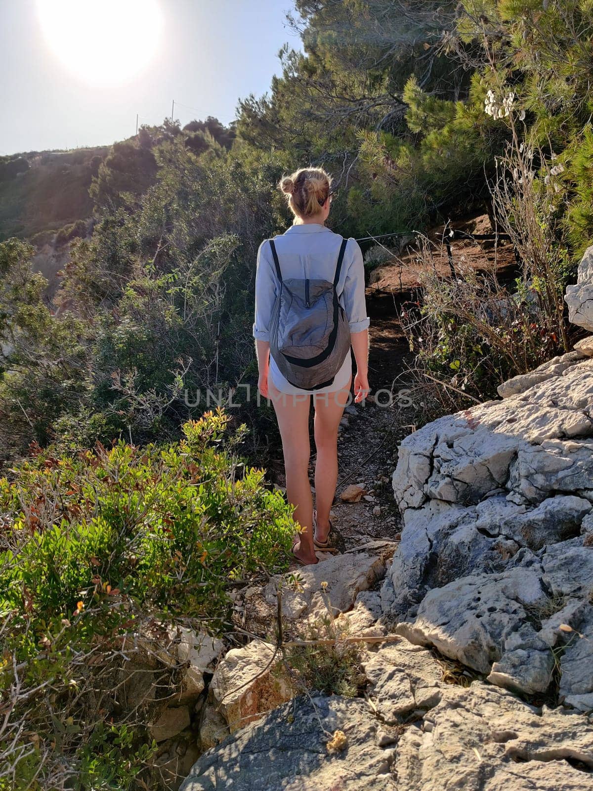 Young active feamle tourist wearing small backpack walking on coastal path among pine trees looking for remote cove to swim alone in peace on seaside in Croatia. Travel and adventure concept.