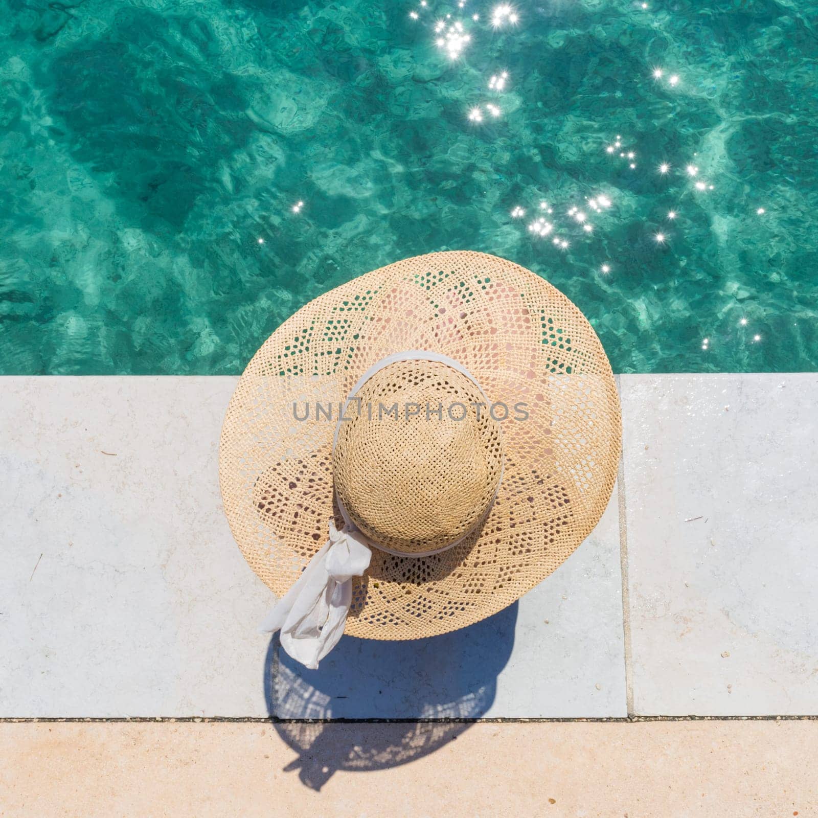 Graphic image of top down view of woman wearing big summer sun hat relaxing on pier by clear turquoise sea.