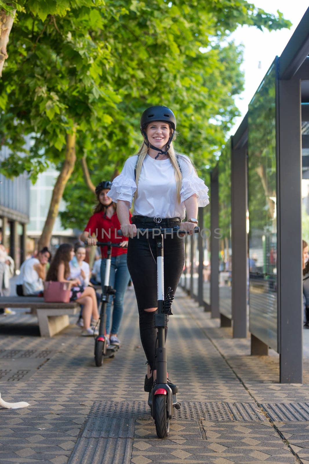 Trendy fashinable teenager girls riding public rental electric scooters in urban city environment. New eco-friendly modern public city transport in Ljubljana, Slovenia.