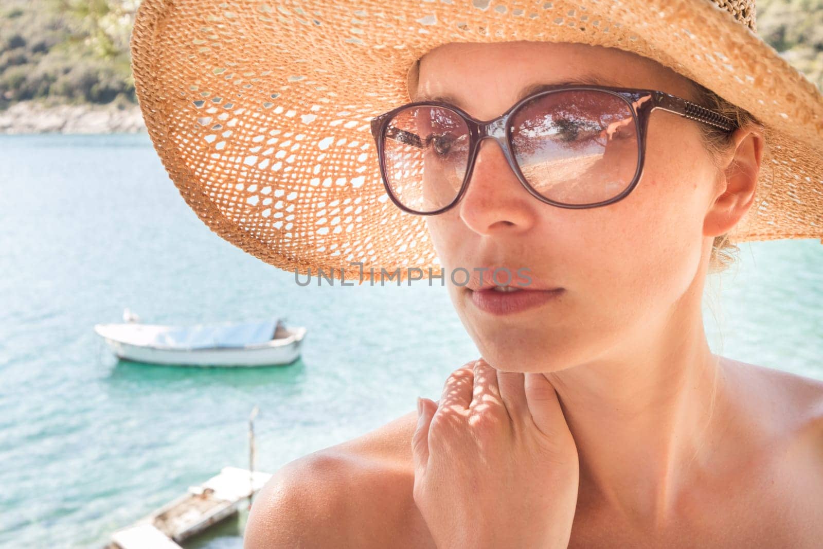 Close up portrait of no makeup natural beautiful sensual woman wearing straw sun hat and sunglasses on the beach in shade of a pine tree.