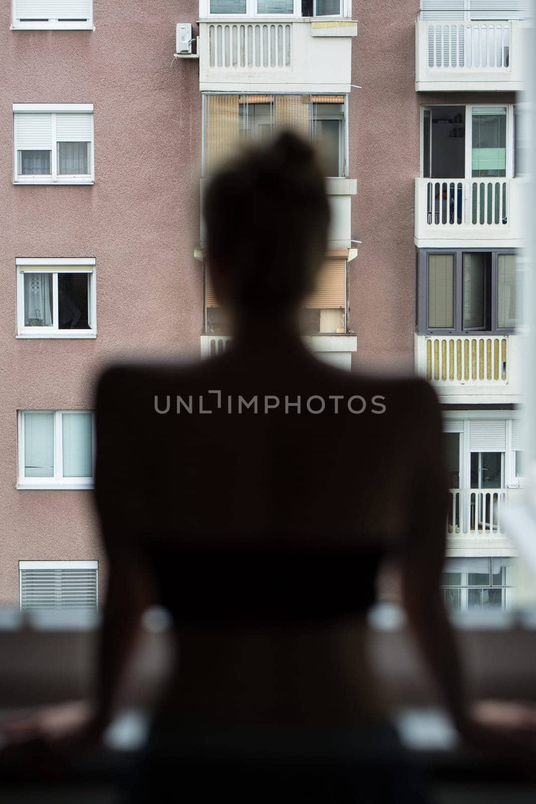 Home quarantine and social distancing during covid pandemic. Silhouette of lonley caucasian woman standing by window, anxiously looking out. Coronavirus infection, pandemics, disease outbreaks.