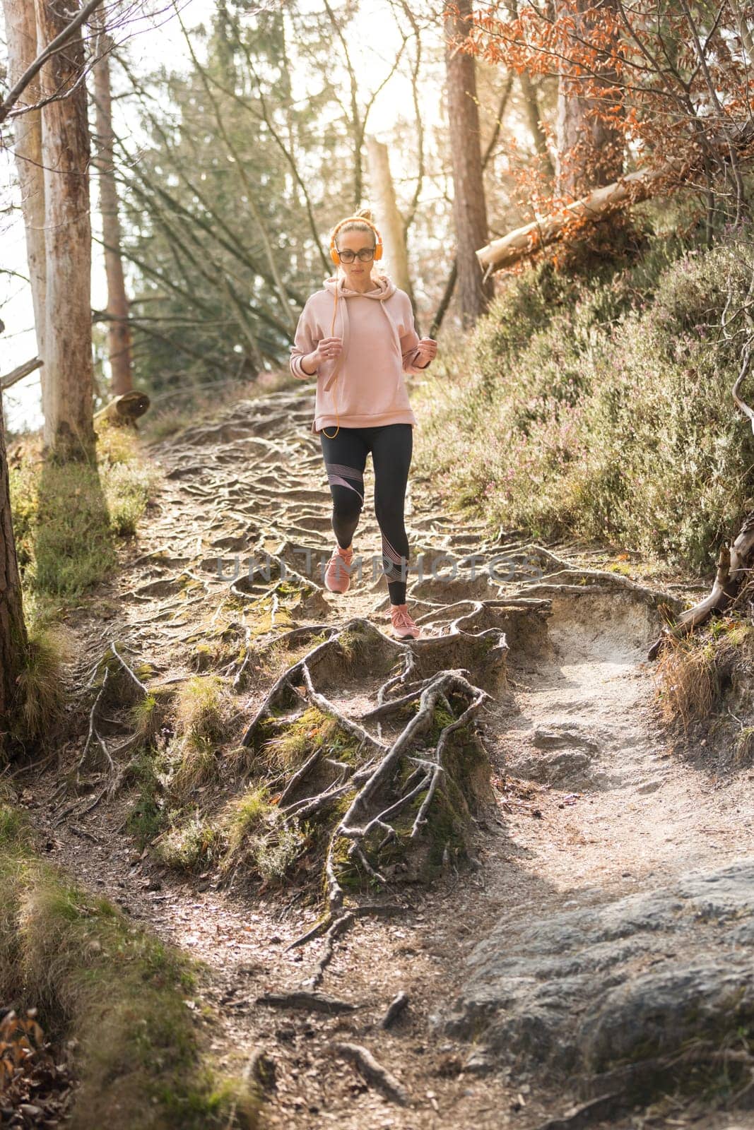 Active sporty woman listening to the music while running in autumn fall forest. Female runner training outdoor. Healthy lifestyle image of young caucasian woman jogging outside.