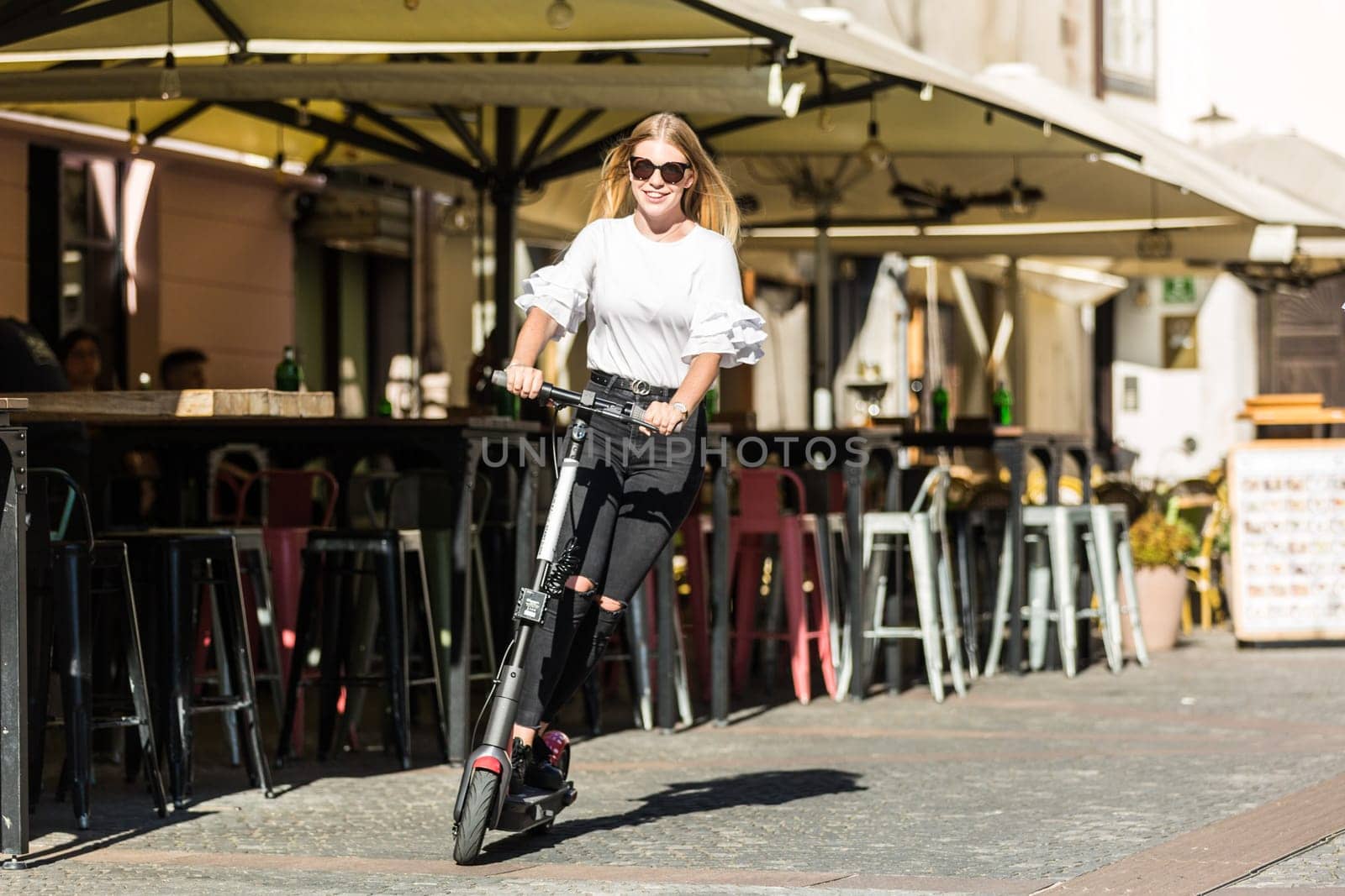 Trendy fashinable teenager girls riding public rental electric scooters in urban city environment. New eco-friendly modern public city transport in Ljubljana, Slovenia.