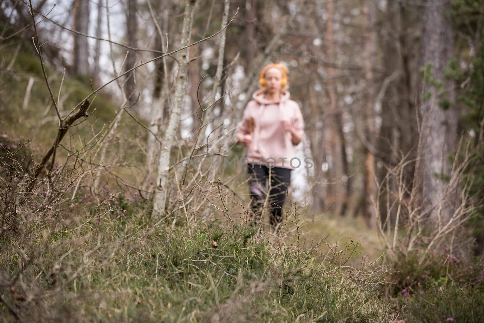 Active sporty woman listening to the music while running in autumn fall forest. Female runner training outdoor. Healthy lifestyle image of young caucasian woman jogging outside.