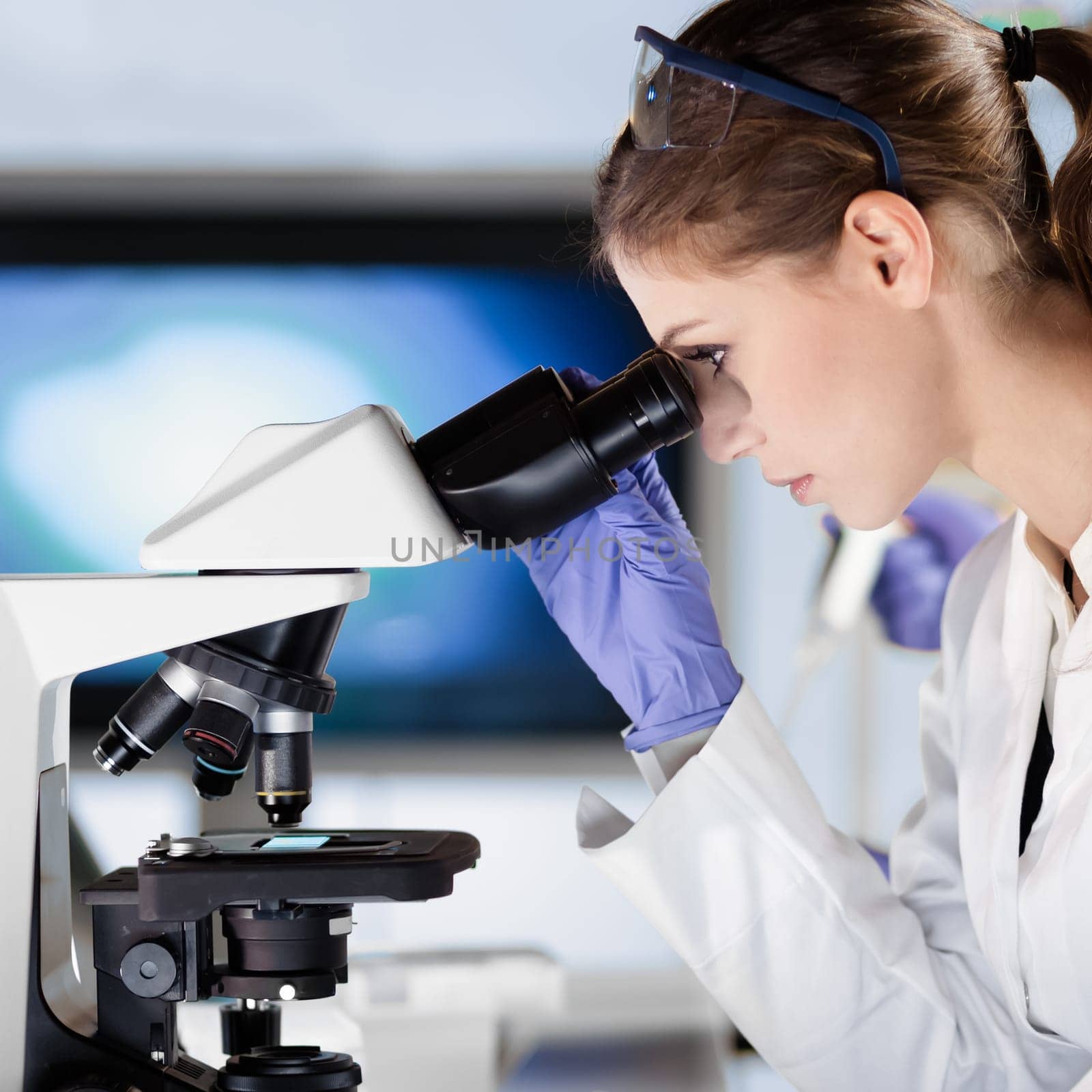 Life scientists researching in laboratory. Attractive female young scientist microscoping in their working environment. Healthcare and biotechnology.