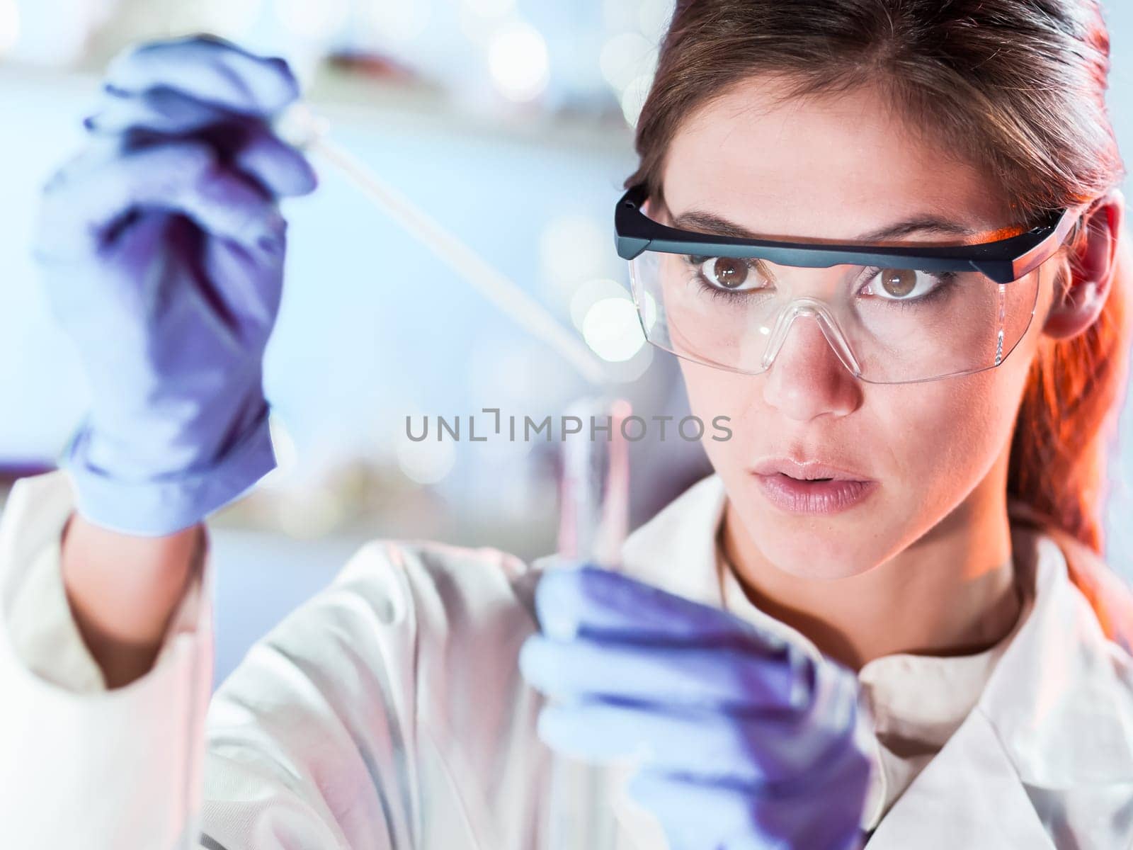 Life scientists researching in laboratory. Focused female life science professional pipetting solution into the glass cuvette. Lens focus on researcher's eyes. Healthcare and biotechnology concept.