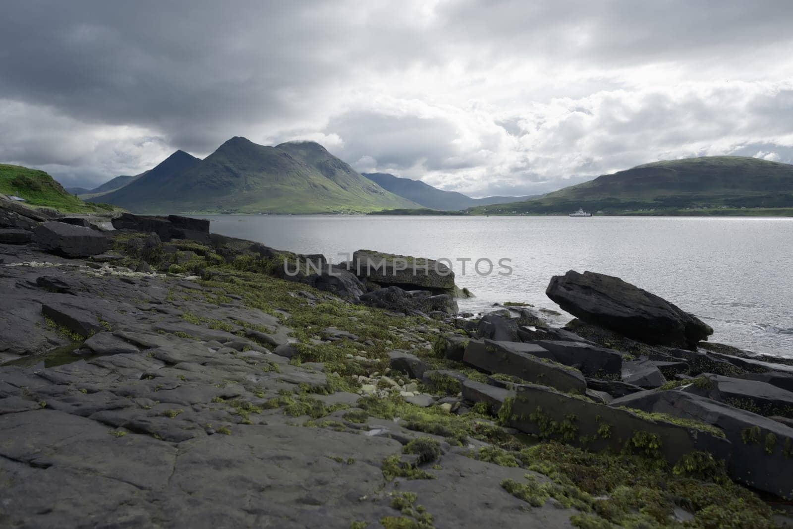 Coastal landscape from the isle of raasay looking towards the isle of skye. Ferry travels the sea under the peak of Glamaig which is cloud topped.