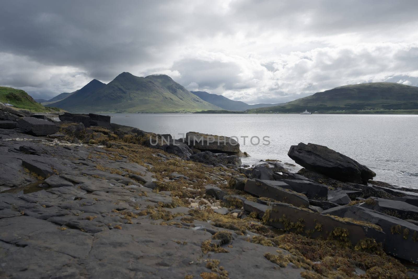 Coastal landscape from the isle of raasay looking towards the isle of skye. Ferry travels the sea under the peak of Glamaig which is cloud topped.
