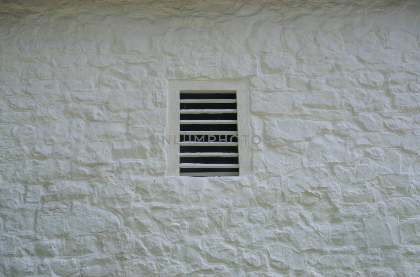 Old slatted ventilation window in a whitewashed stone wall on historic farm. Full frame rustic image in natural light with copy space.