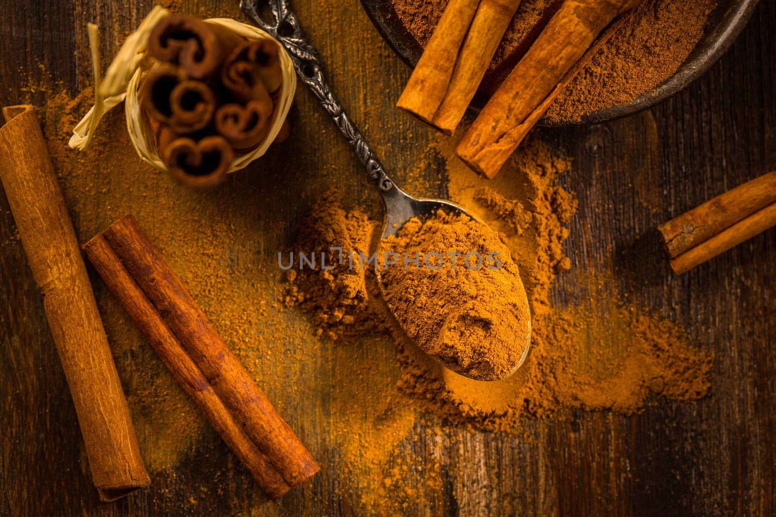 Cinnamon powder in vintage spoon with cinnamon sticks on wooden background as cooking and baking ingredient.