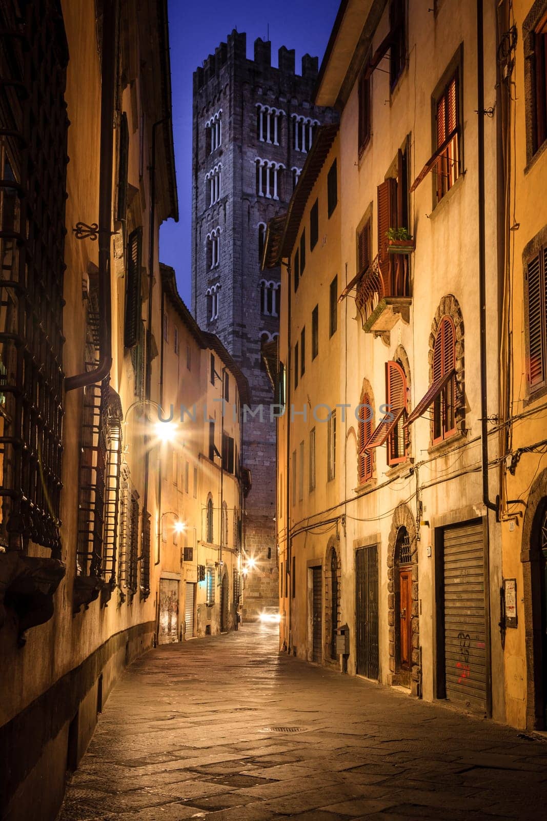 A street in the historic part of Lucca, Italy at night with a view of the Lucca Cathedral tower