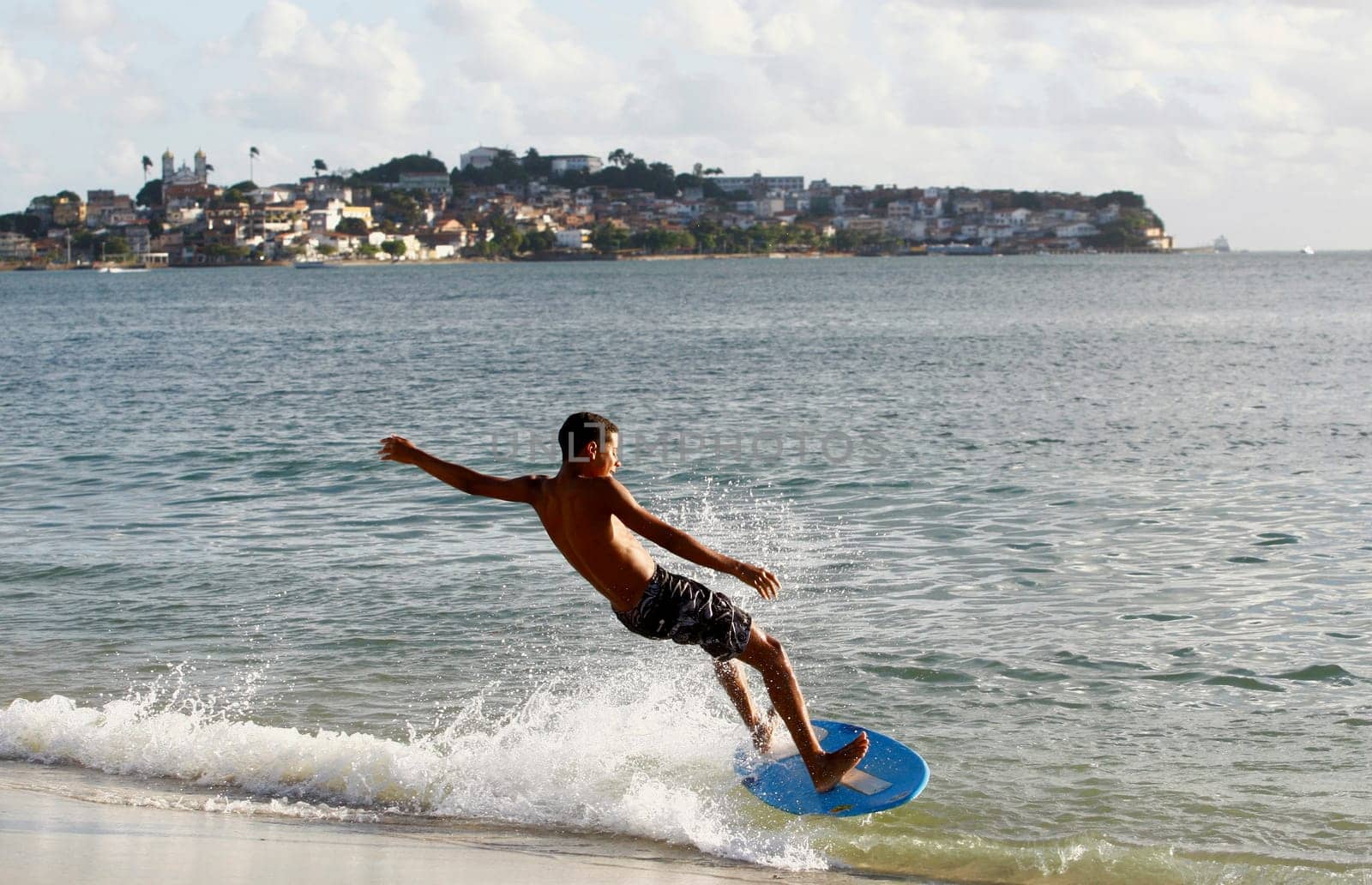 salvador, bahia / brazil - august 12, 2015: young man is seen surfing with a piece of wood on Ribeira beach in the city of Salvador.