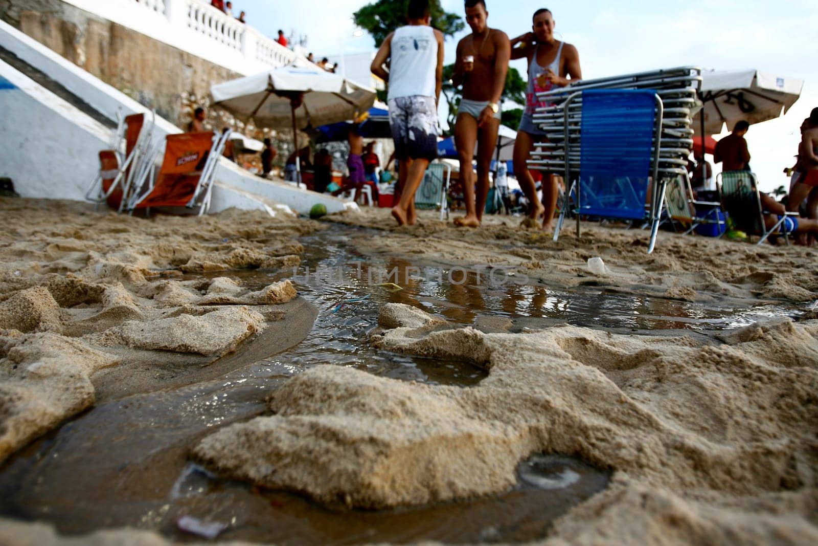 salvador, bahia / brazil - november 4, 2015: people are seen by the open sewage water gushing in the sand of Porto da Barra in the city of Salvador.