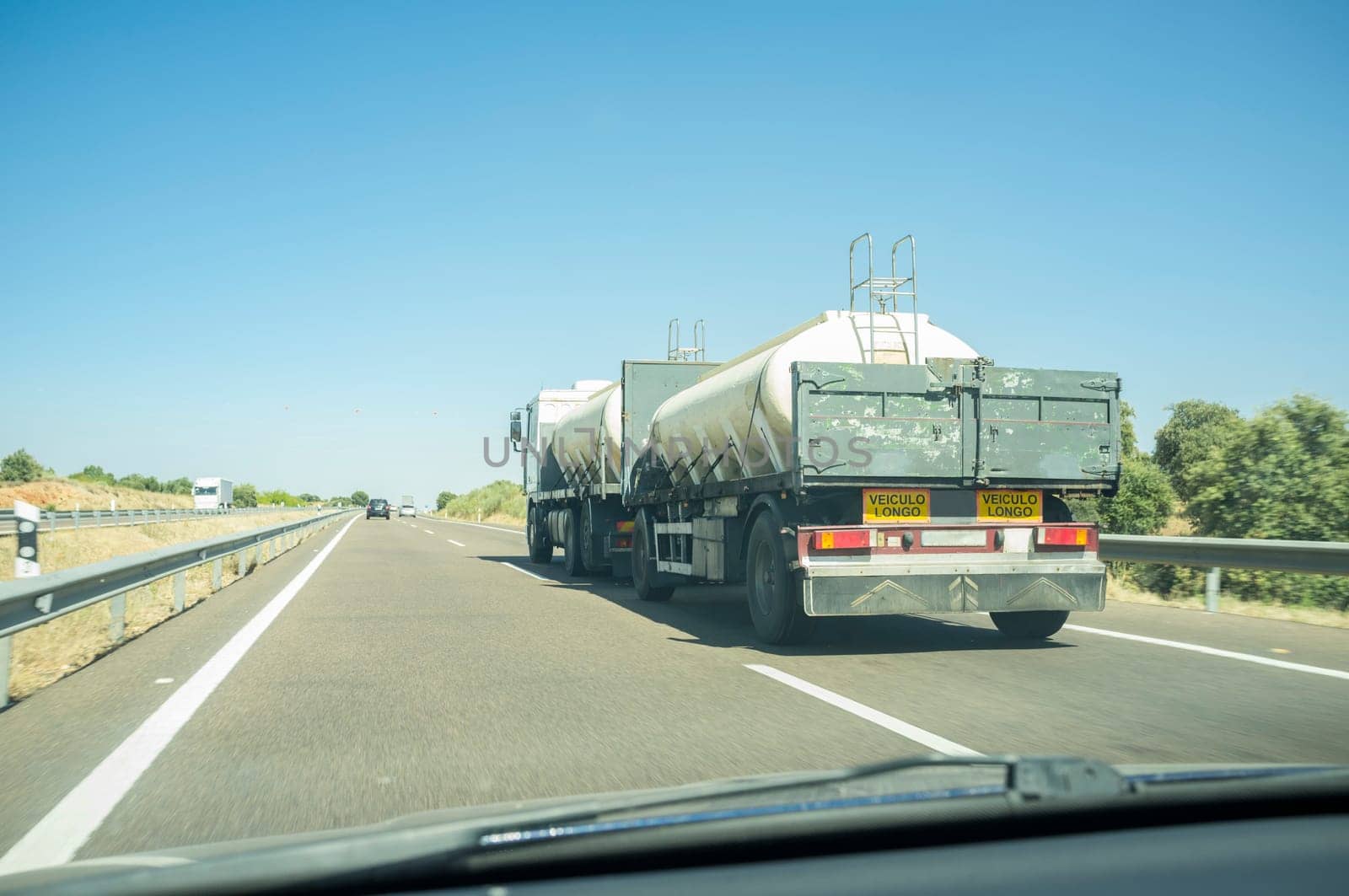 Driving behind B-double trailer loading tanks on divided highway road. View from the inside of the car