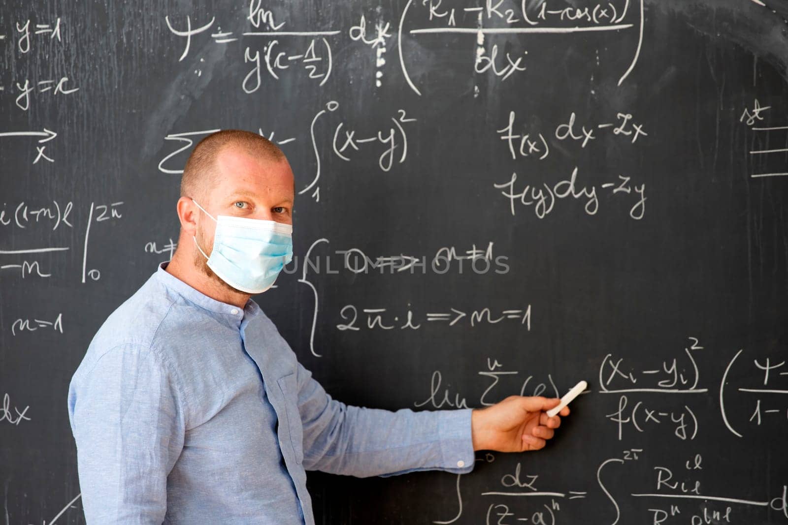 Male teacher with mask teaching math lesson at school. Social distanting and classroom safety during coronavirus epidemic