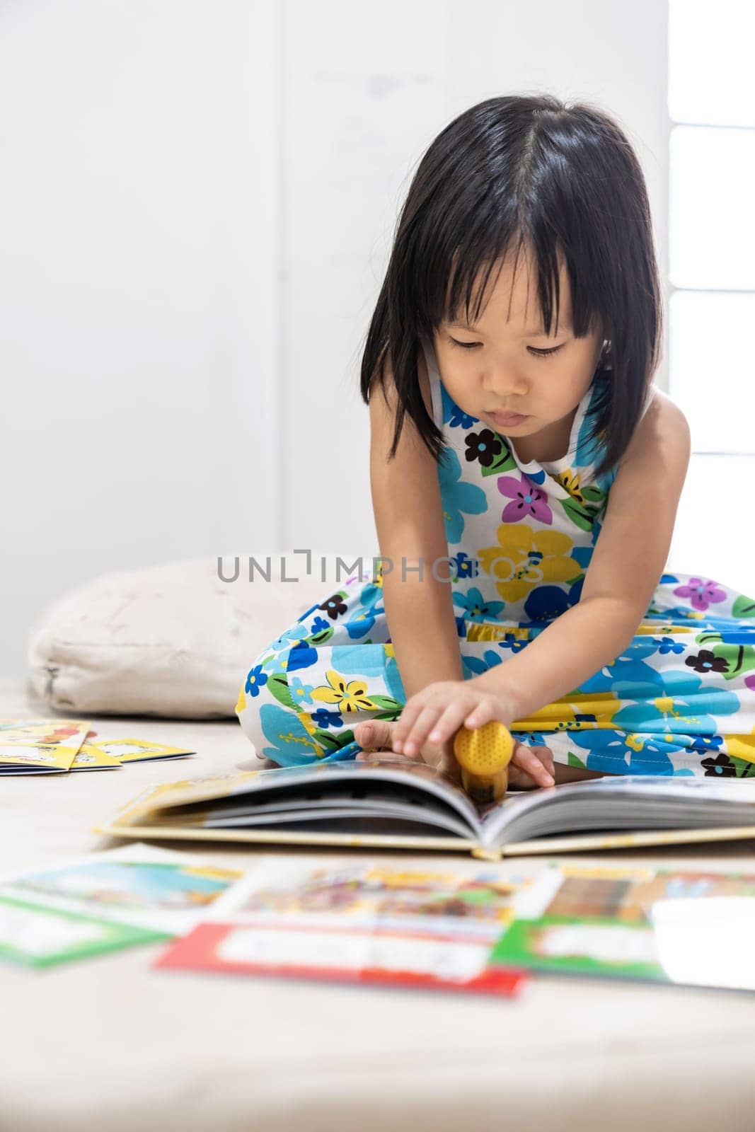 Asian girl child reading interactive book in living room at home as home schooling while city lockdown because of covid-19 pandemic across the world. Home Schooling prepare for Preschool concept.